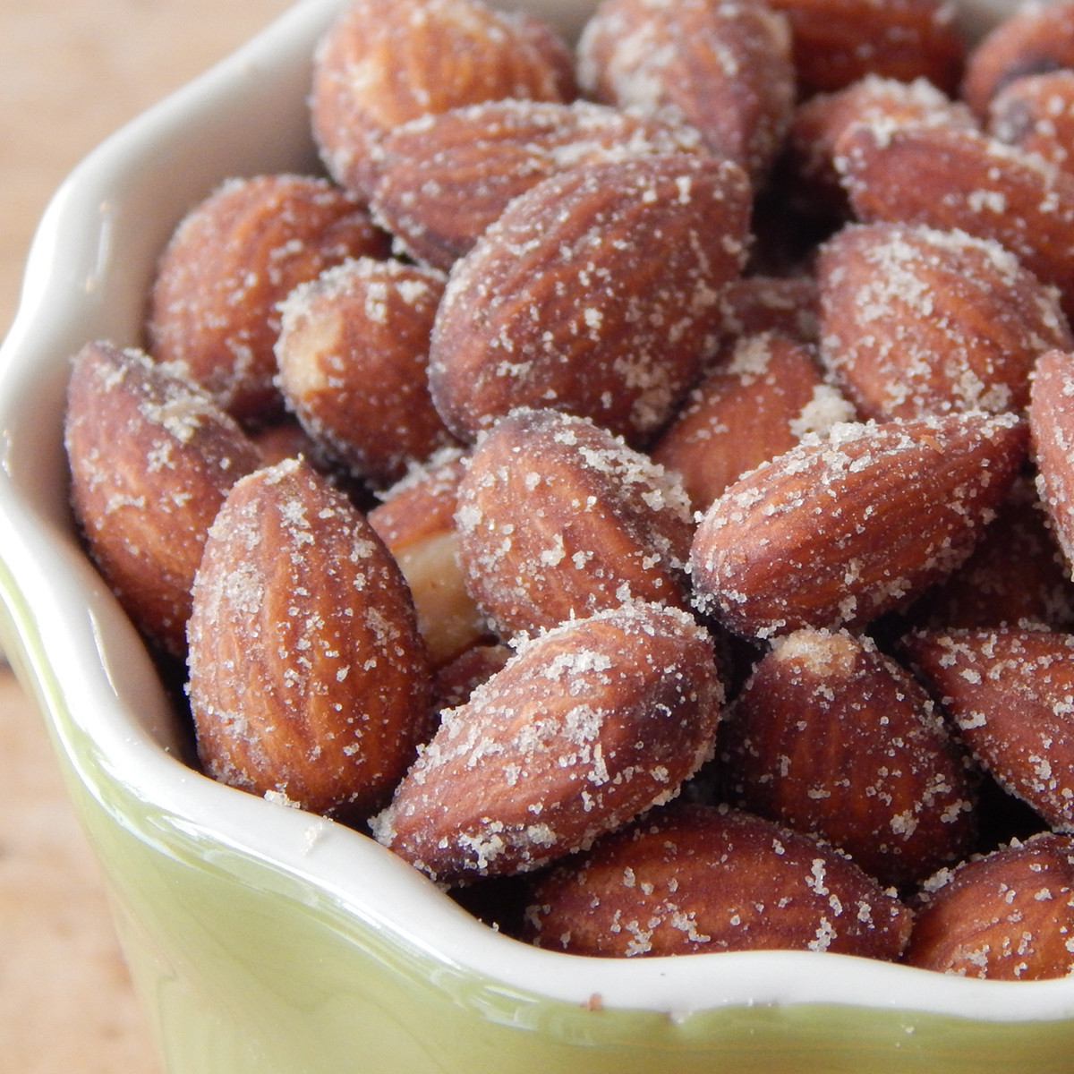 A close-up picture of smoked almonds in a green bowl. The bowl has a wavelike shape and is white on the inside, green on the outside. 