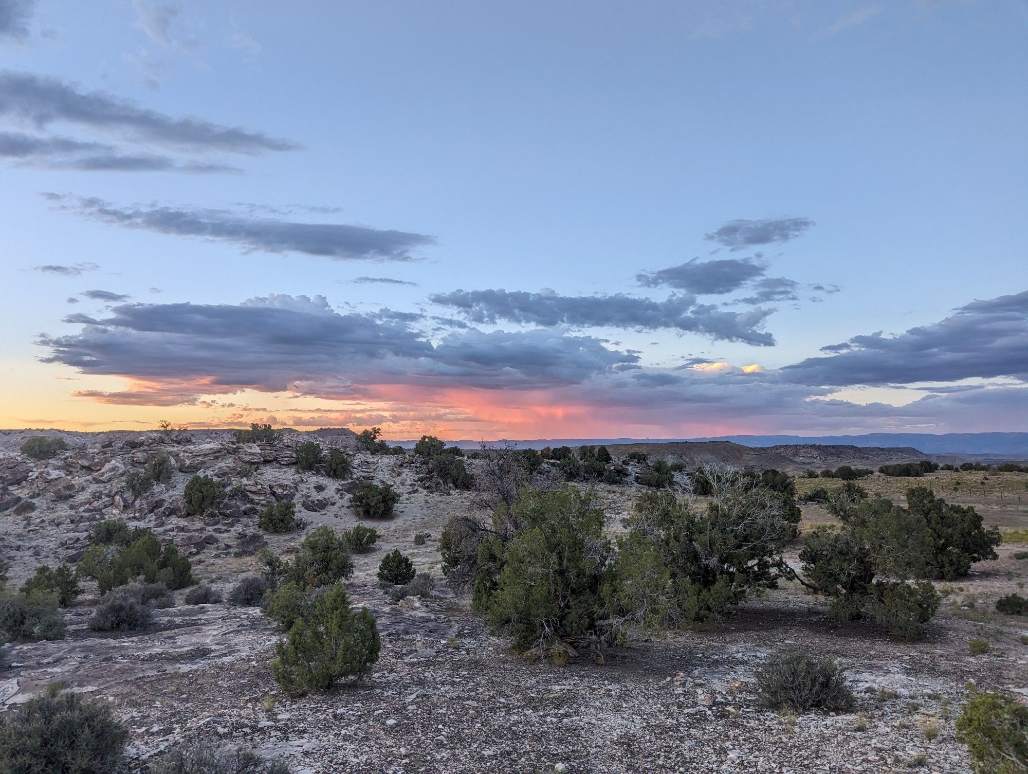 a picture of a desert sunset. colors stretch from yellow to orange to red to purple with plenty of blue sky and broad, low, flat clouds across the landscape. 