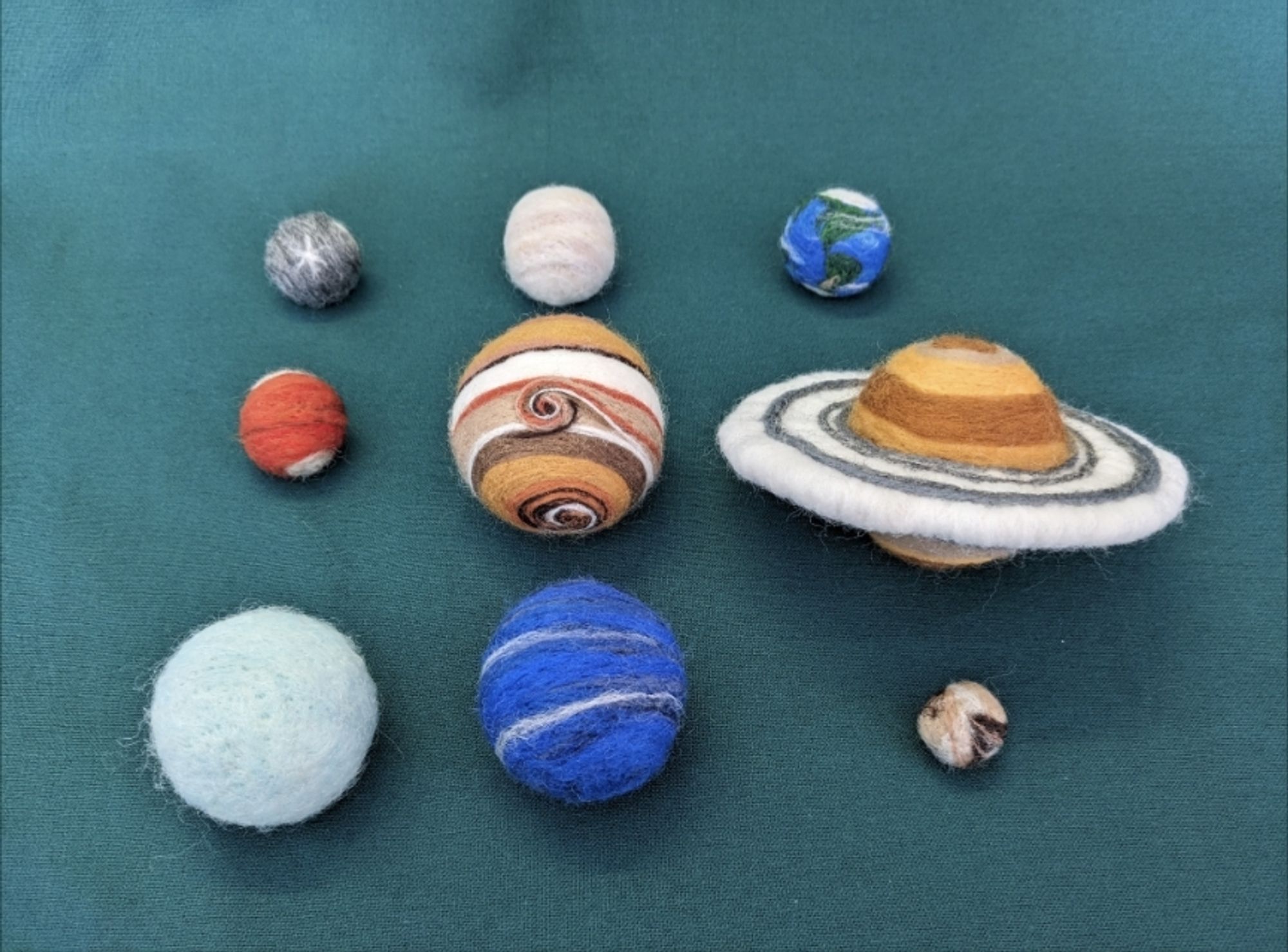 The nine planets of our solar system, rendered in wool, sit on a green background