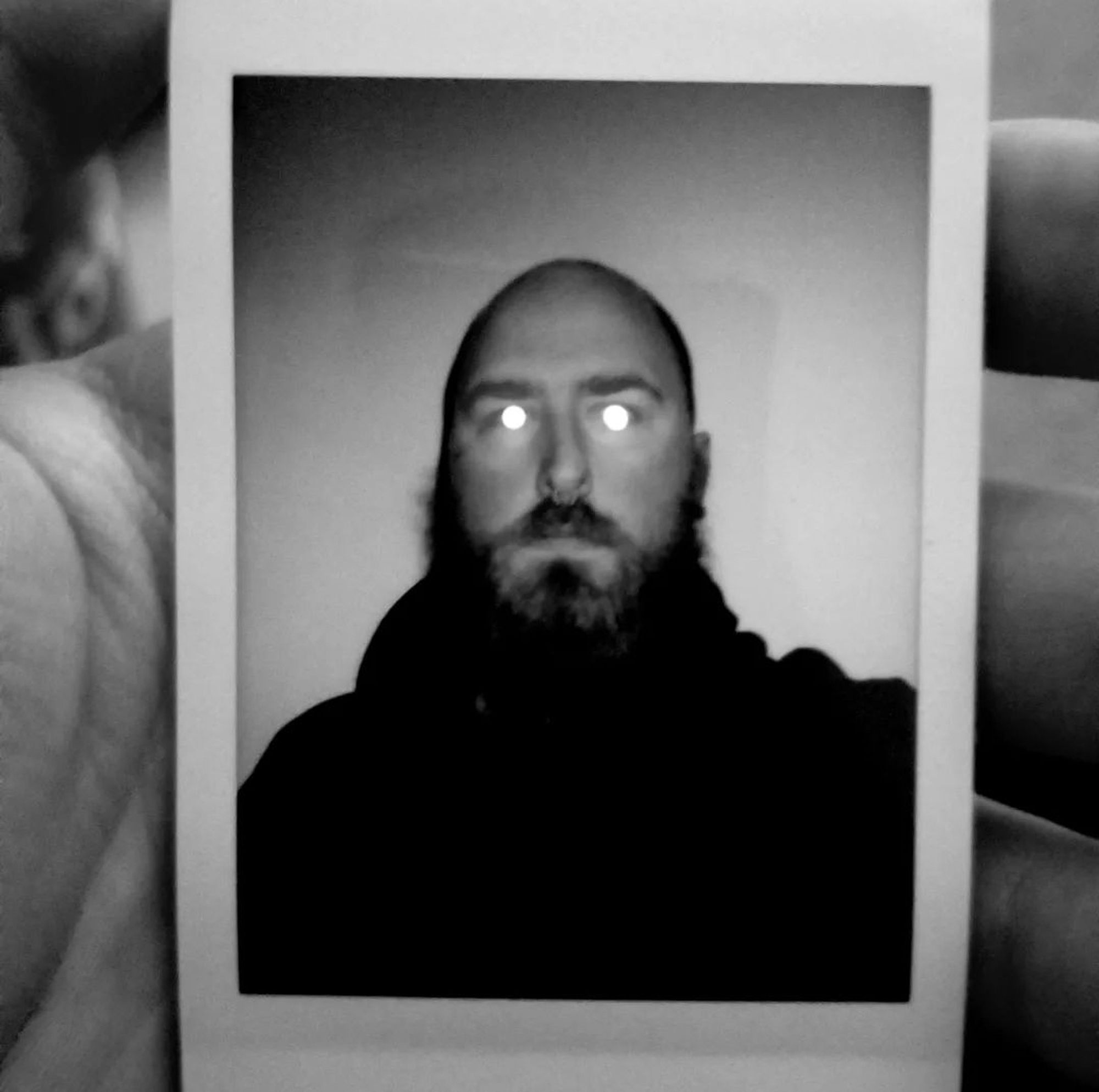 A hand holding a Polaroid image of a man with glowing eyes.