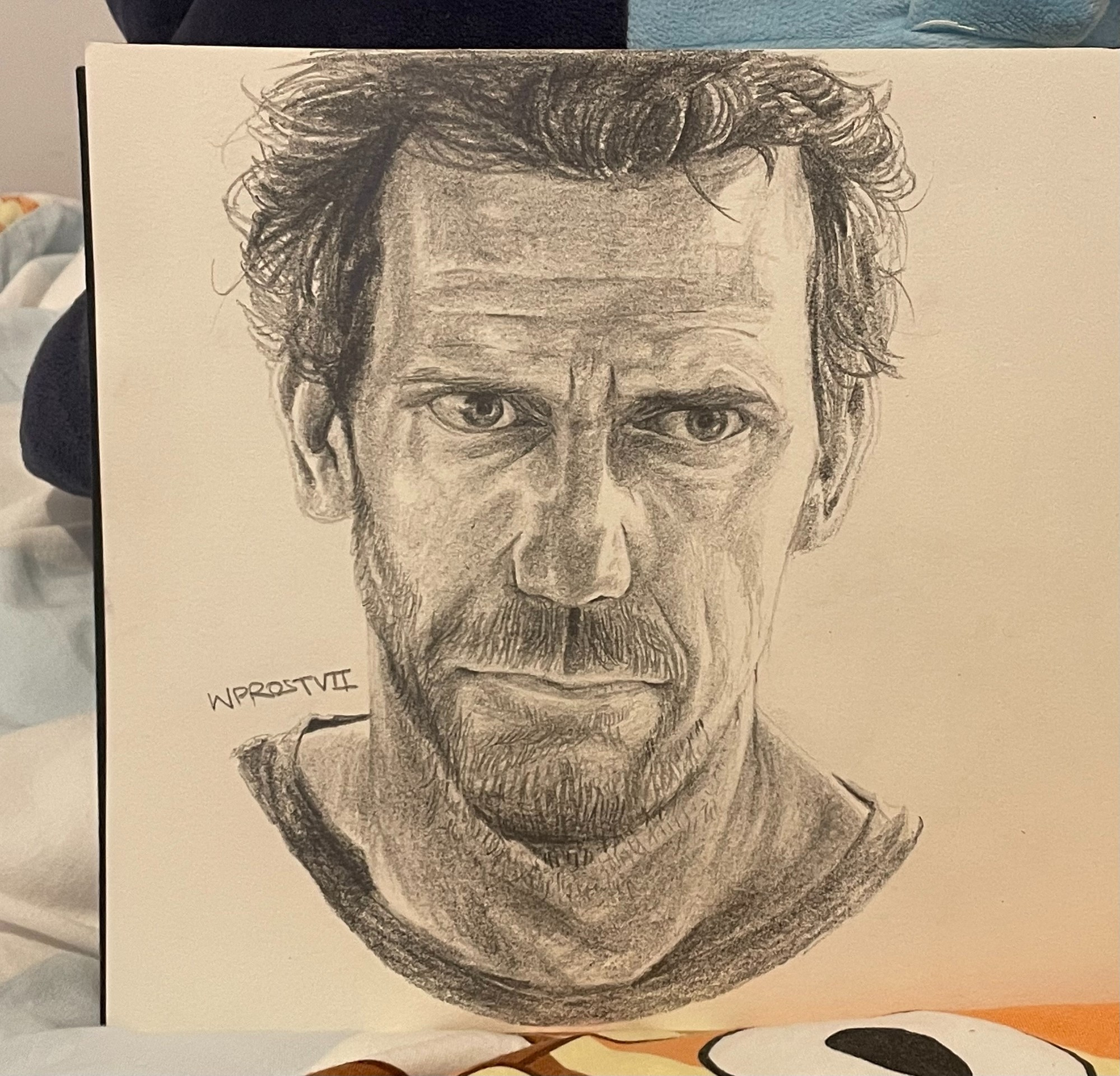 A traditional black and white portrait of a fictional character named Dr House from the series House MD, drawn with a HB and a 4B pencil.
In this drawing, the character is looking in front with a serious facial expression depicting slight annoyance. He has scruffy hair and an untrimmed slight stubble.