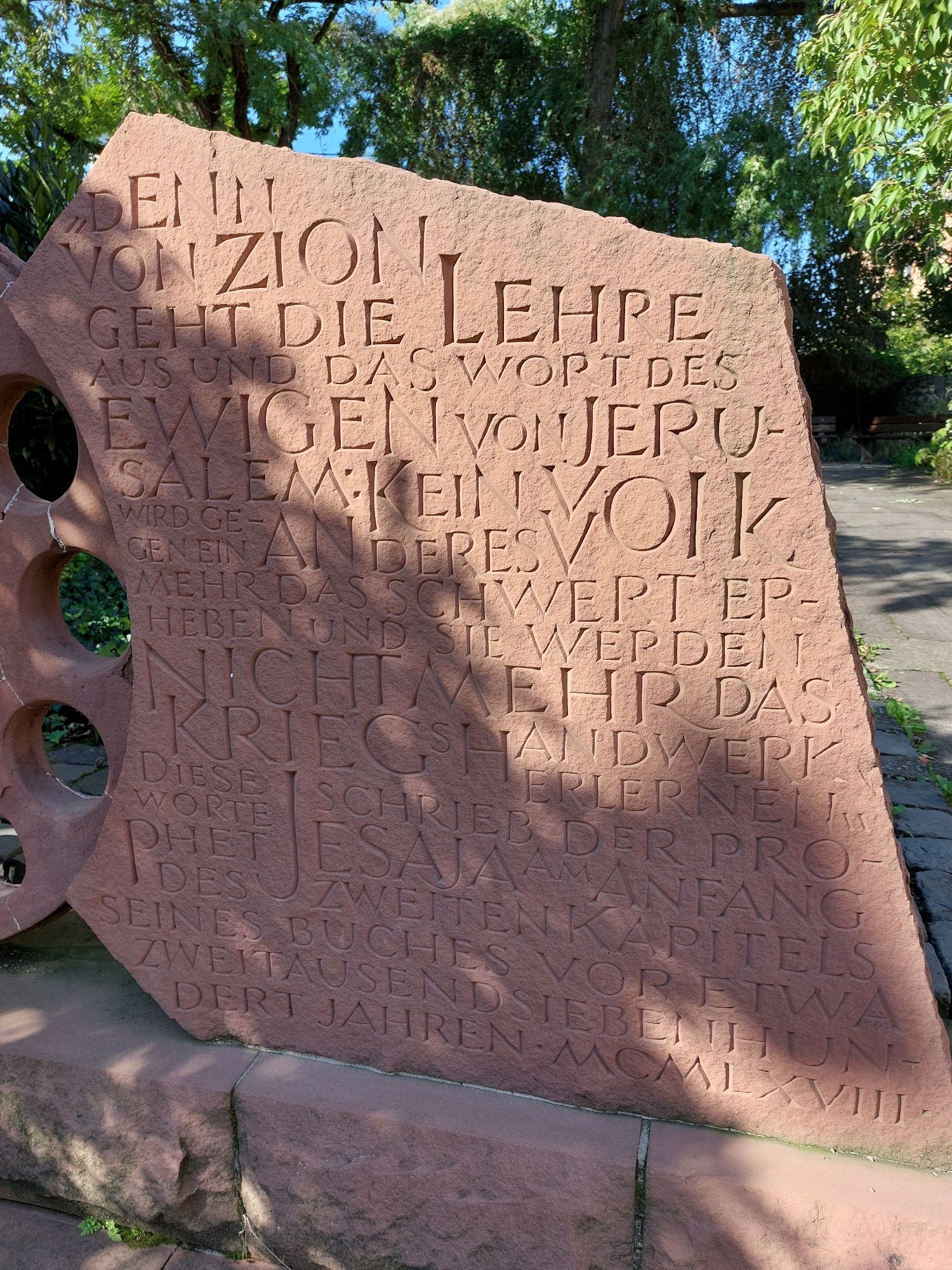 Inschrift auf der rechten Seite:
"Denn von Zion geht die Lehre aus und das Wort des Ewigen von Jerusalem: Kein Volk wird gegen ein anders Volk mehr das Schwert erheben und sie werden nicht mehr das Kriegshandwerk erlernen." Diese Worte schrieb der Prophet Jesaja am Anfang des zweiten Kapitels seines Buches vor etwa zweitausendsiebenhundert Jahren • MCMLXVIII •