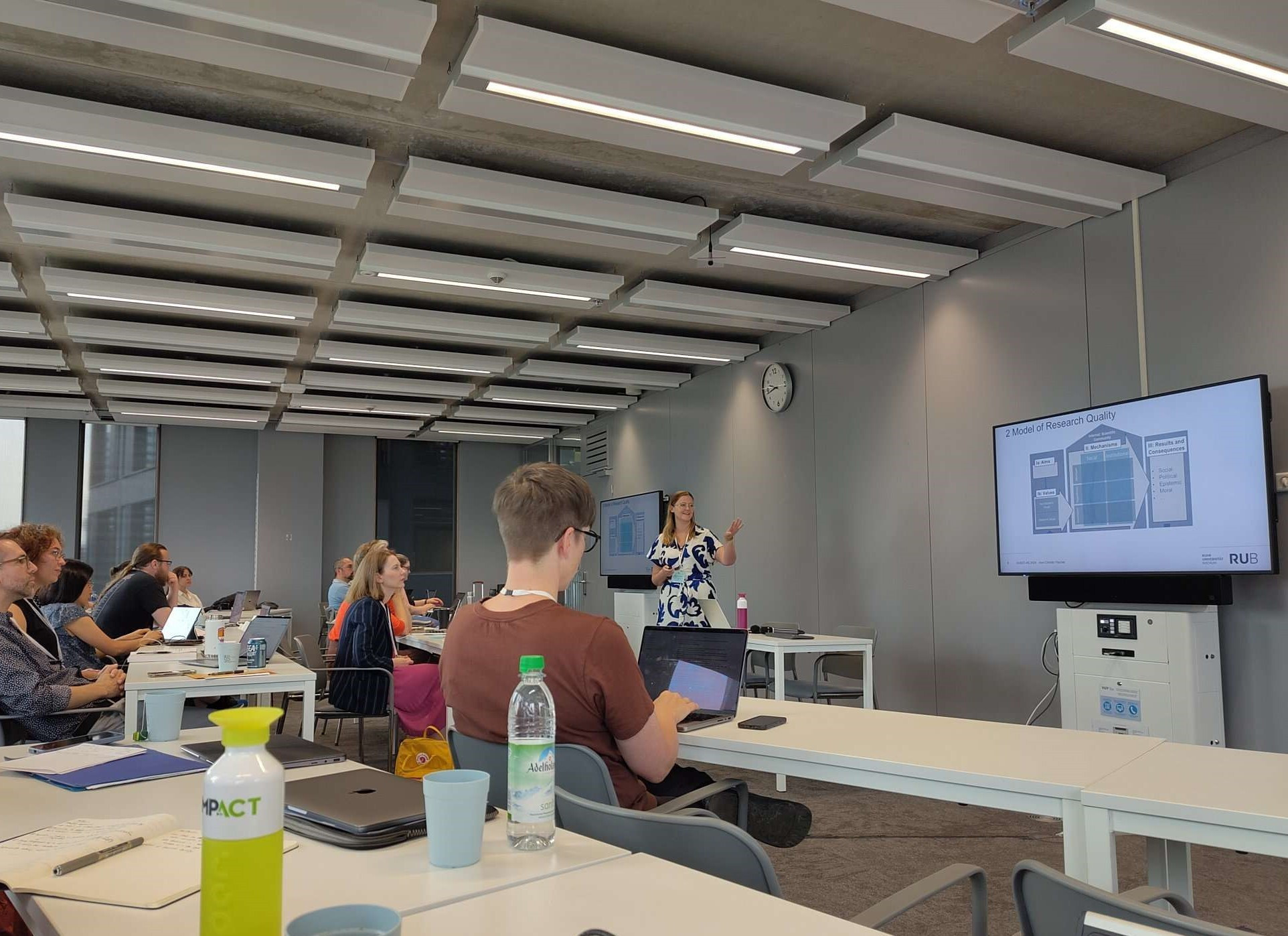 Ann-Christin Fischer standing in front of an audience next to a screen showing a model of research quality.