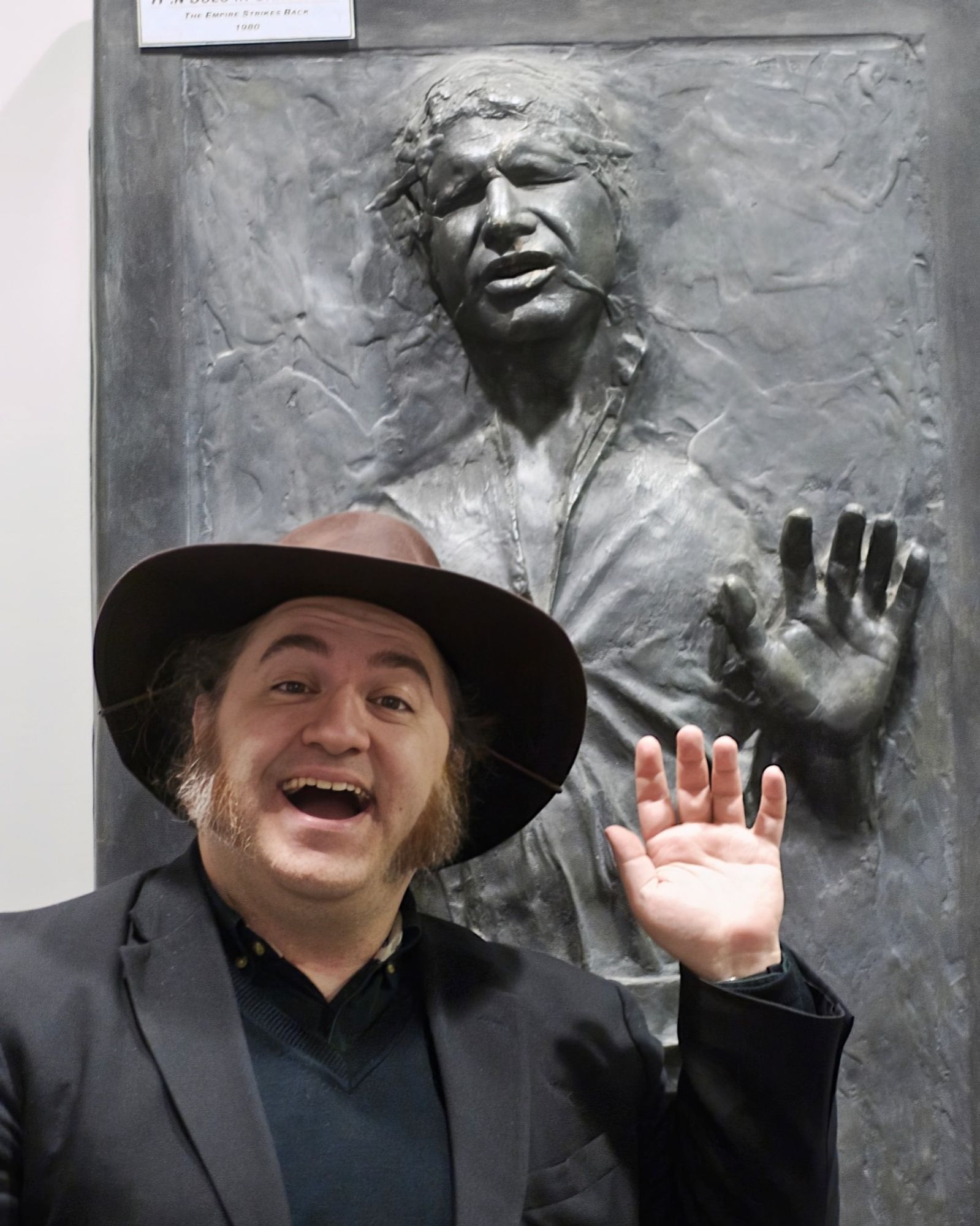 Me in an office hallway, standing in front of the "Han Solo In Carbonite" prop from "The Empire Strikes Back." I am smiling and waving in a way that mimics Han's frozen pose.