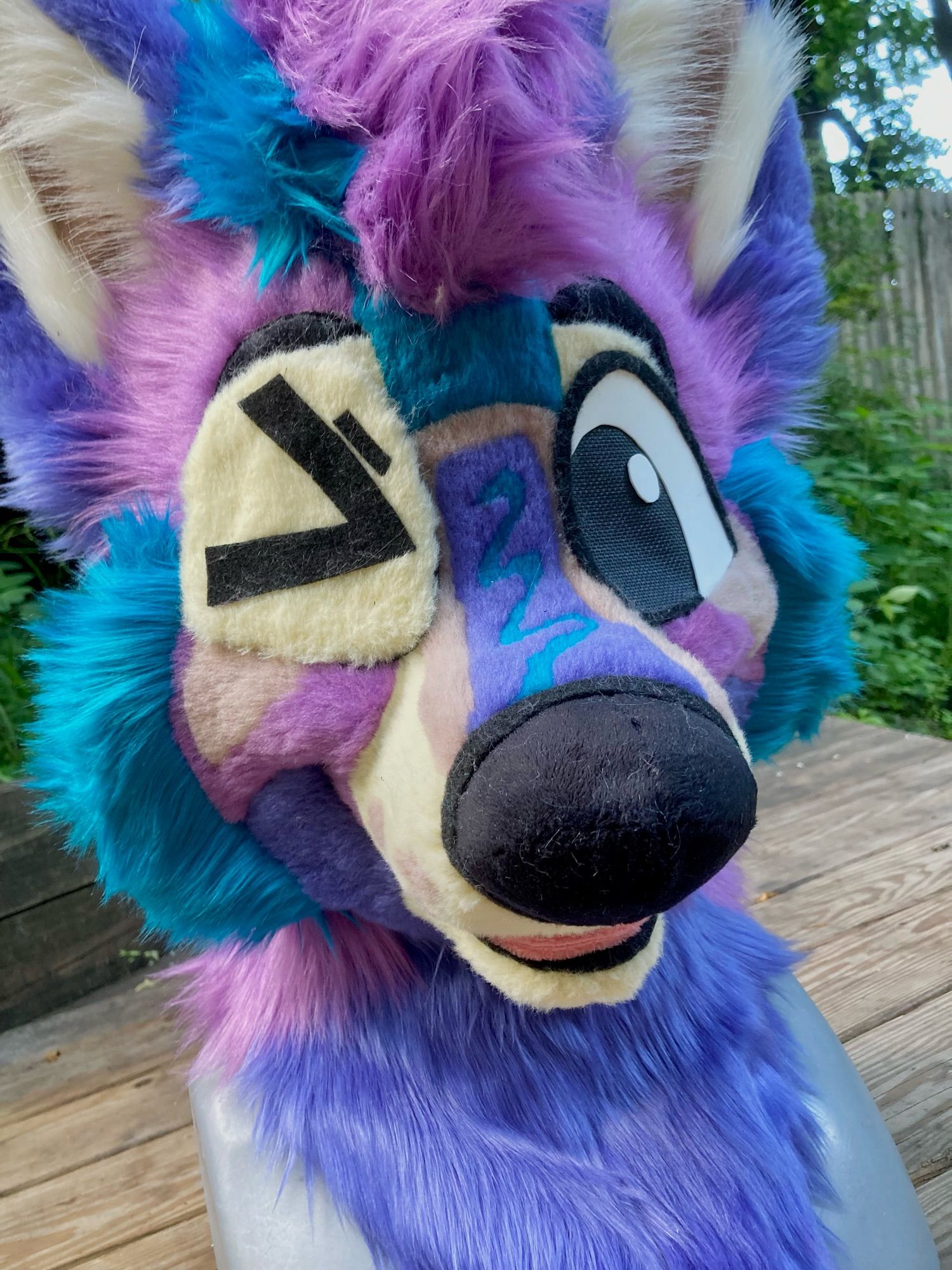 A photo of a happy toony wildberry poptart inspired wolf fursuit head. He is on a mannequin head outside and is winking at the camera because of a squinty eyelid