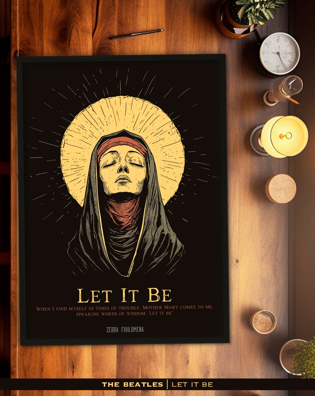 A imagem mostra um pôster estilizado da música "Let It Be" dos Beatles. O pôster apresenta uma figura que remete à iconografia religiosa, com uma mulher de olhos fechados, envolta em um véu, em uma pose serena e com um halo dourado ao fundo. Abaixo, aparece o título da música "Let It Be", com a citação: "When I find myself in times of trouble, Mother Mary comes to me, speaking words of wisdom, 'Let it be'", referenciando a famosa letra da canção. N aparte inferior, há o logo da loja Zebra Filomena. O pôster está emoldurado e colocado sobre uma mesa de madeira.