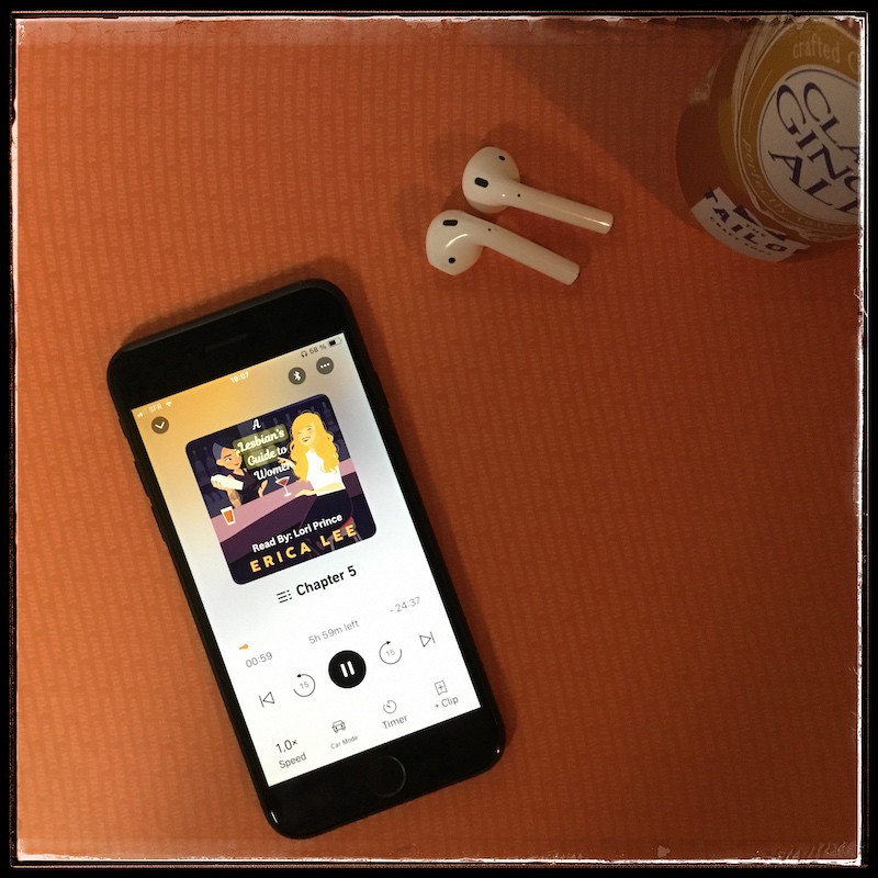 On an orange background, an iPhone with the cover of A Lesbian's Guide to Women by Erica Lee, narrated by Lori Prince next to a pair of AirPods and a can of ginger ale.