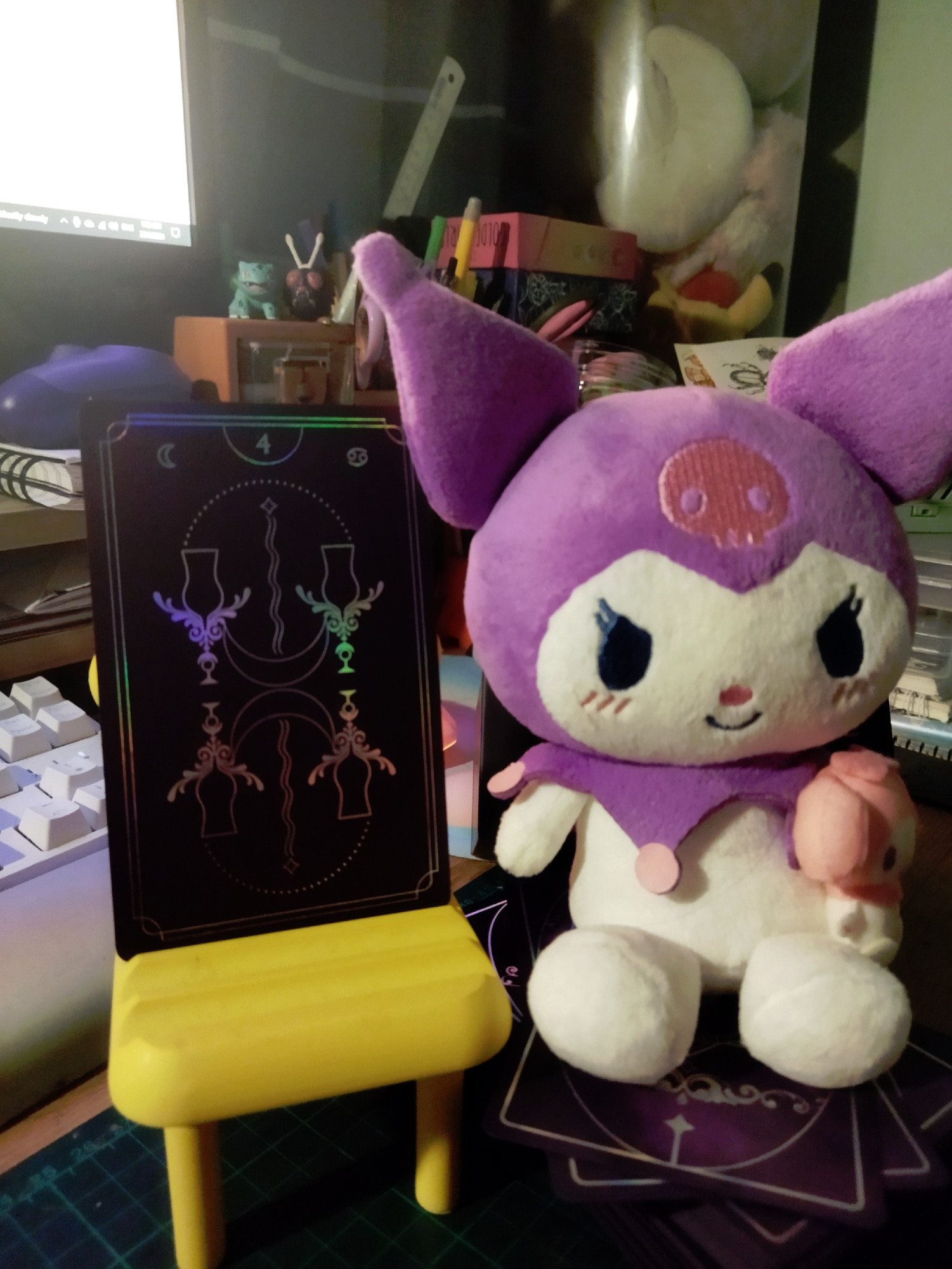 A tarot card on a mini yellow chair stand. A Kuromi plushie next to it.