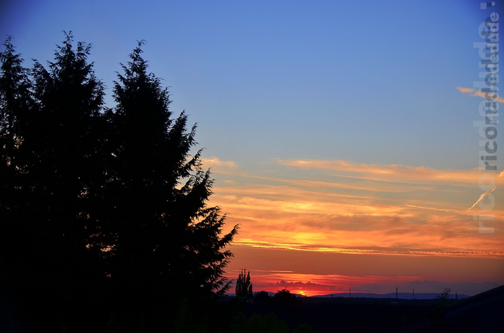 FOTO eigen

Das Bild zeigt die Qualität der Fotografie mit einer DSLR-Kamera im Vergleich zu Software-korrigierter Knipserei mit einem mobilen Telefon.

Aufgenommen aus dem Dachfenster, nach Westen gerichtet. Der Himmel im oberen Bilddrittel ist Mittelblau. In der horizontalen Bildmitte überwiegt schleierartige Bewölkung, die durch die rot-glühend untergehende Sonne angestrahlt wird. Am linken Bildrand drei Bäume, die im Gegenlicht schwarz erscheinen.