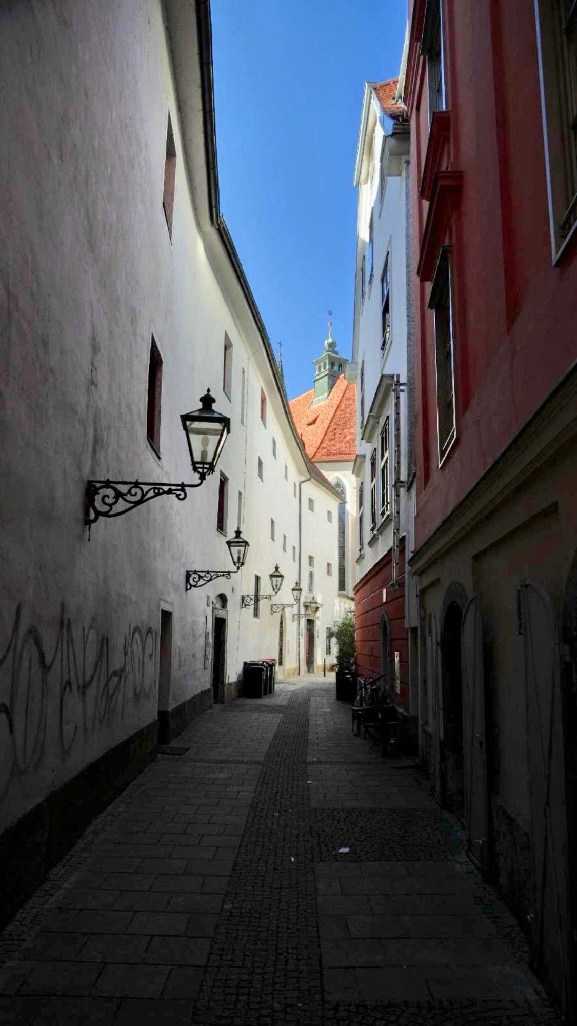 Blick durch die enge Stainzergasse in Richtung Franziskanerplatz
Altstadt Ensemble im sogenannten Kälbernen Viertel
die Reihe der Laternen weist zum Bildzentrum, welches durch den Keil des blauen Himmels von Oben und die gepflasterte Gasse von Unten definiert wird