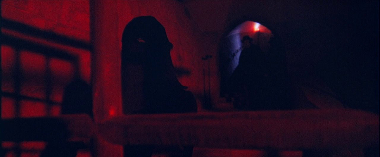 Dark figures in a dungeon lit with red light 