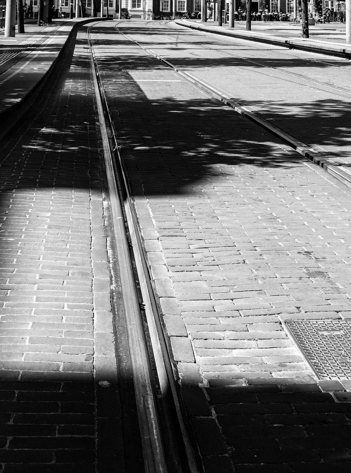 Zwart wit opname.
Tramrails verdwijnen in de verte. Schaduwen vallen over de trambaan.