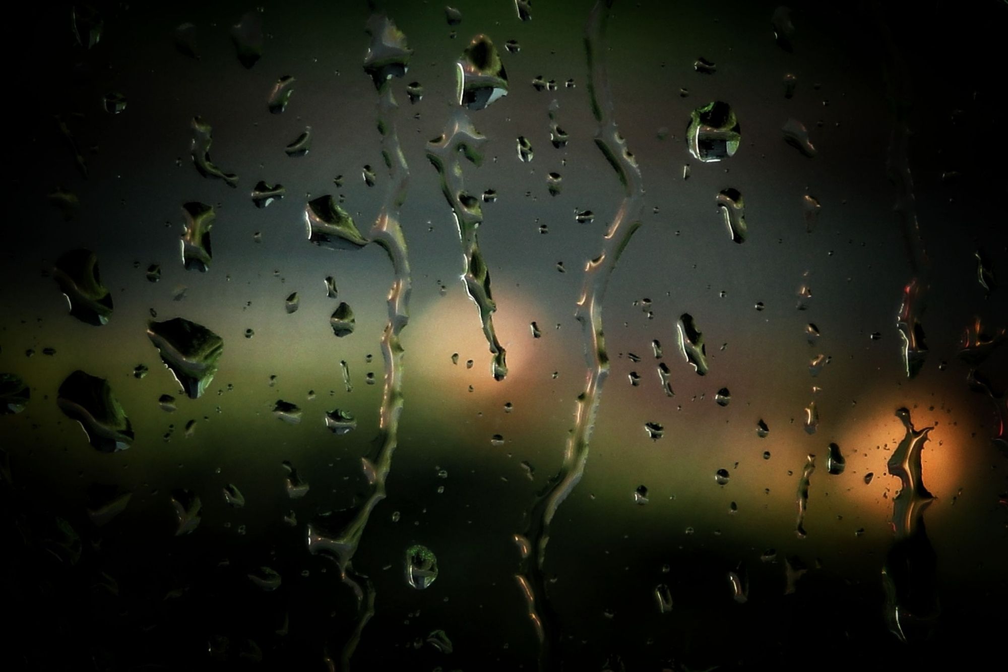 Raindrops on a window. Blurred lights visible in the dark outside.