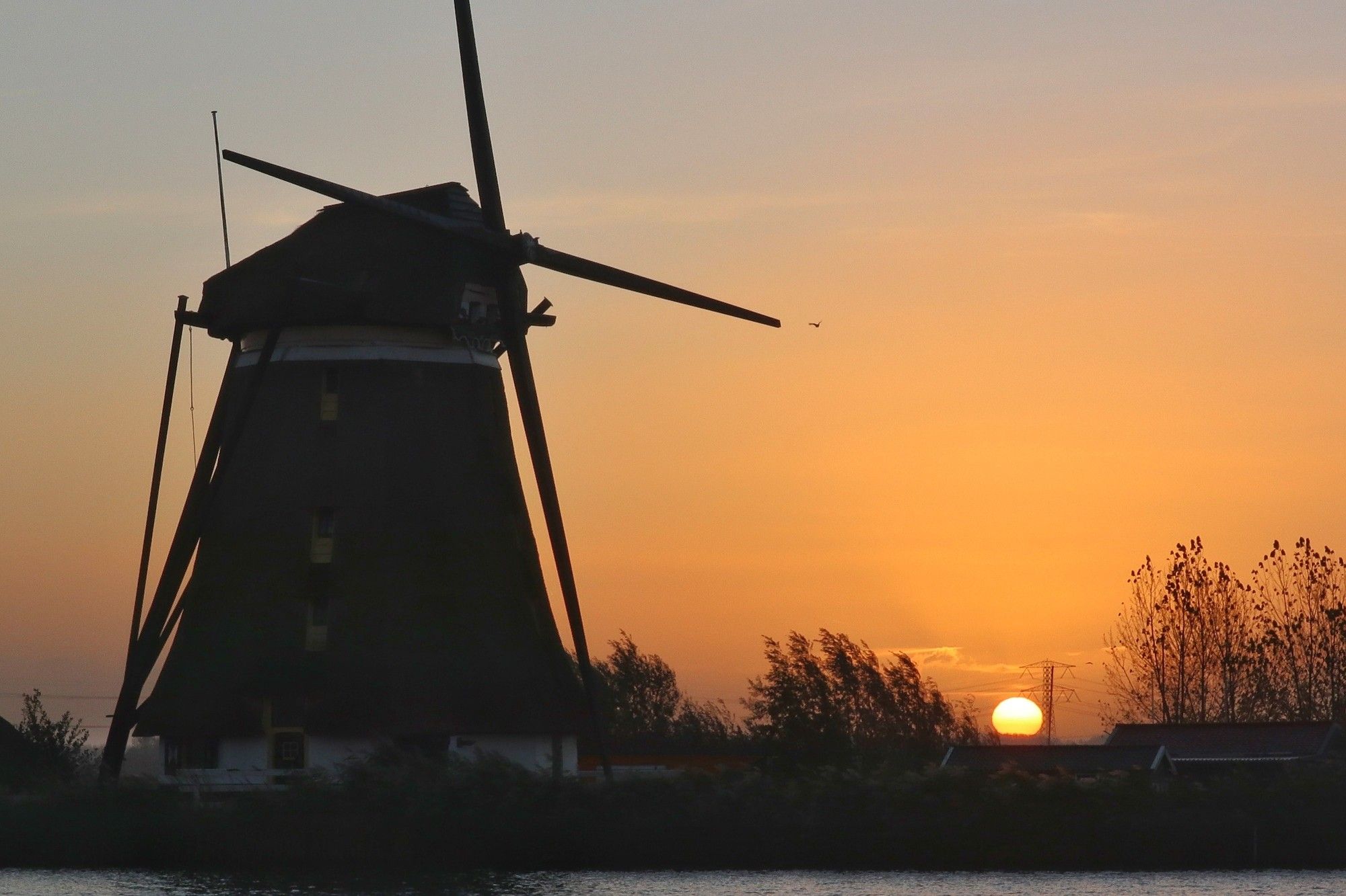 Silhouet van molen tegen een oranje zonsopgang. Zon komt lichtgeel te voorschijn.