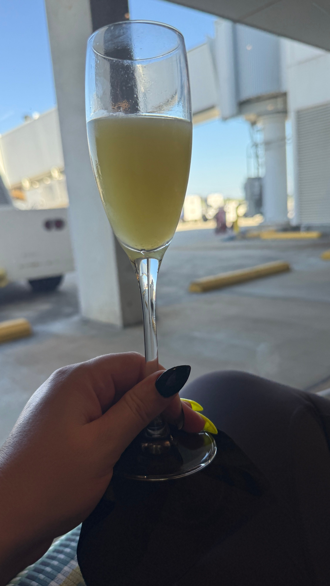 A mimosa in a champagne glass in front of a window below a gate at an airport 