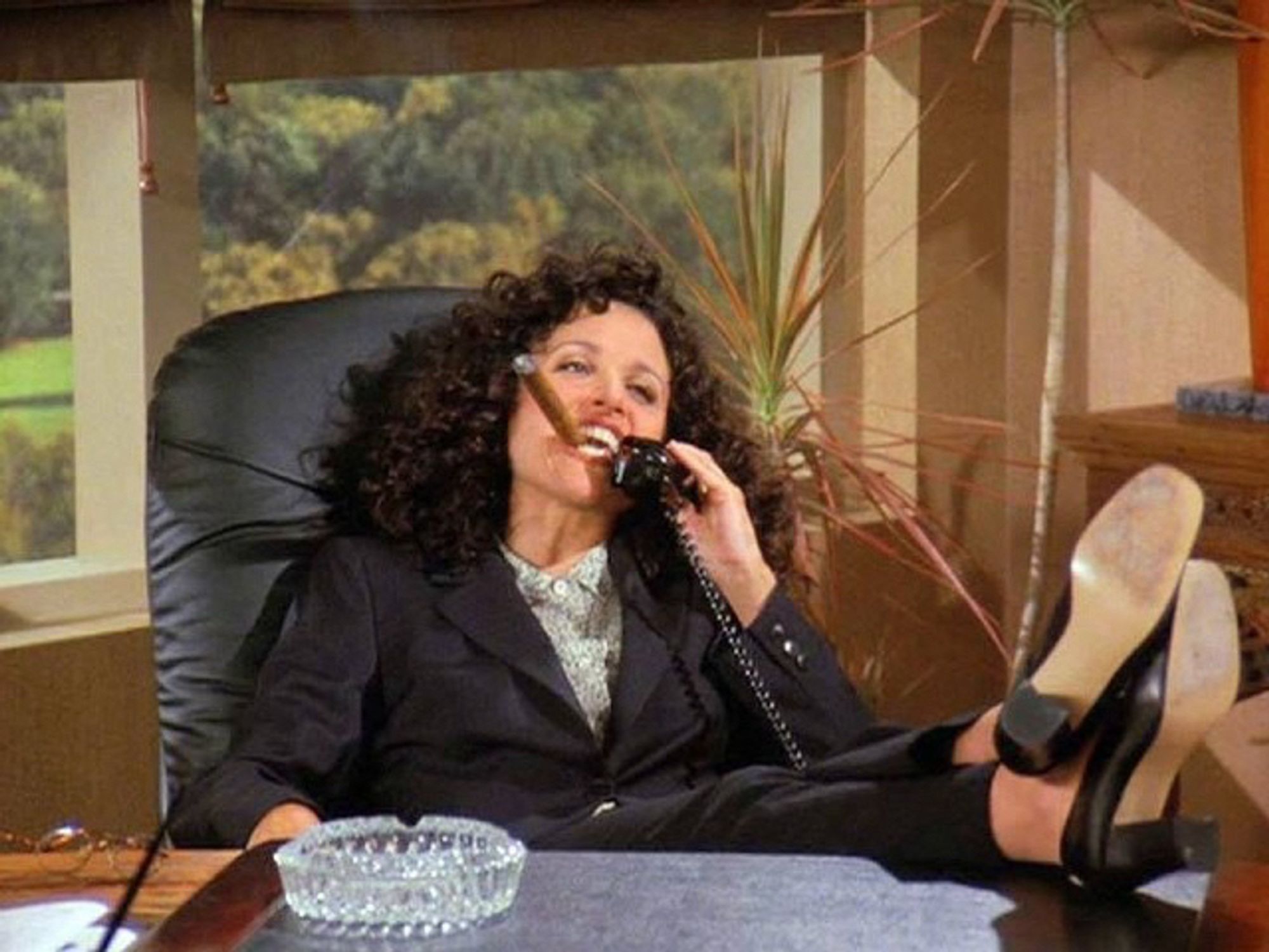 Elaine from the show Seinfeld, leaning back with her feet on a desk, smoking a cigar.