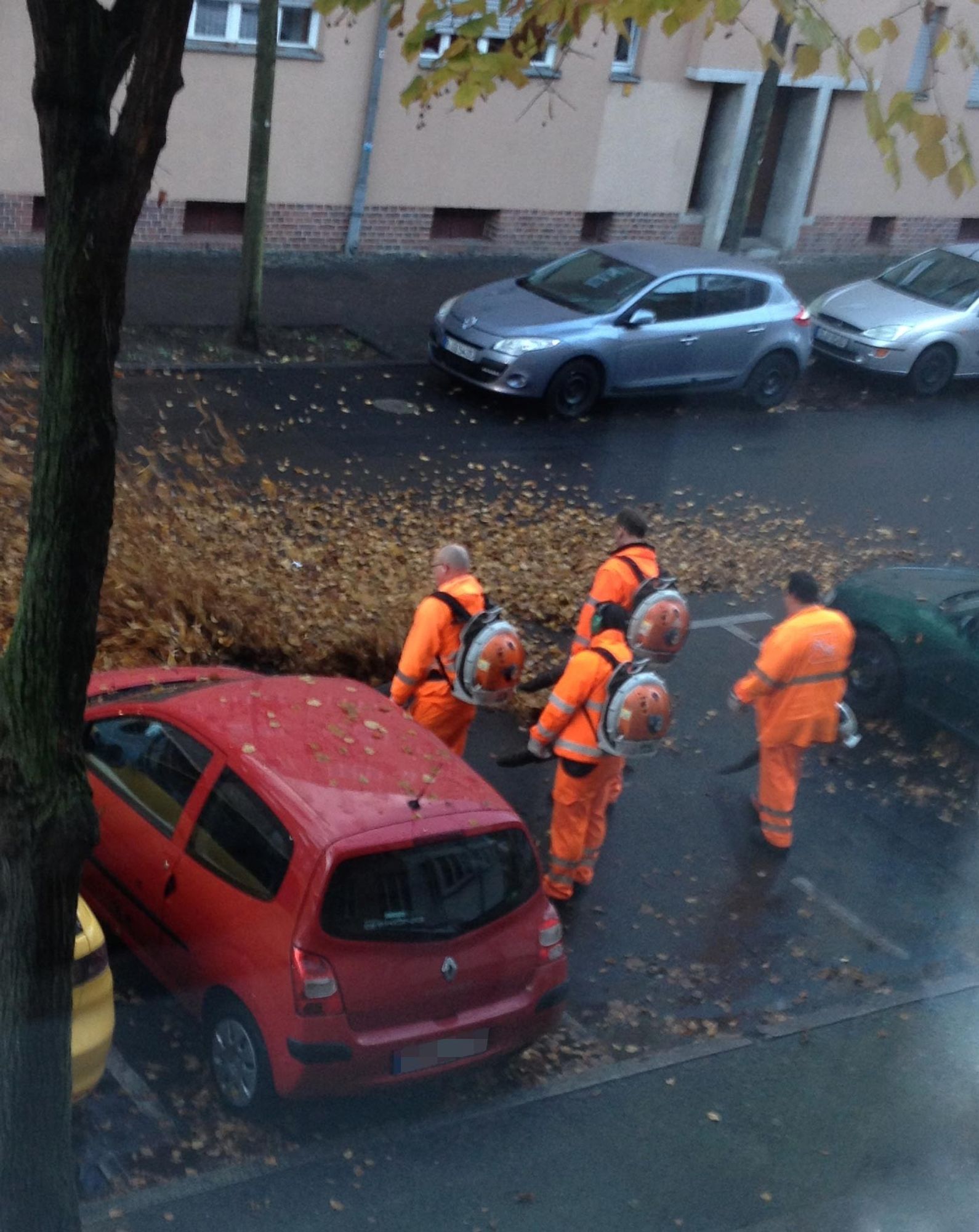 Ein Foto von vier Mitarbeitern der Berliner Stadtreinigung BSR mit Laubbläsern die in einer Art Formation vor meinem alten Bürofenster stehen und das Laub auf die Straße blasen.