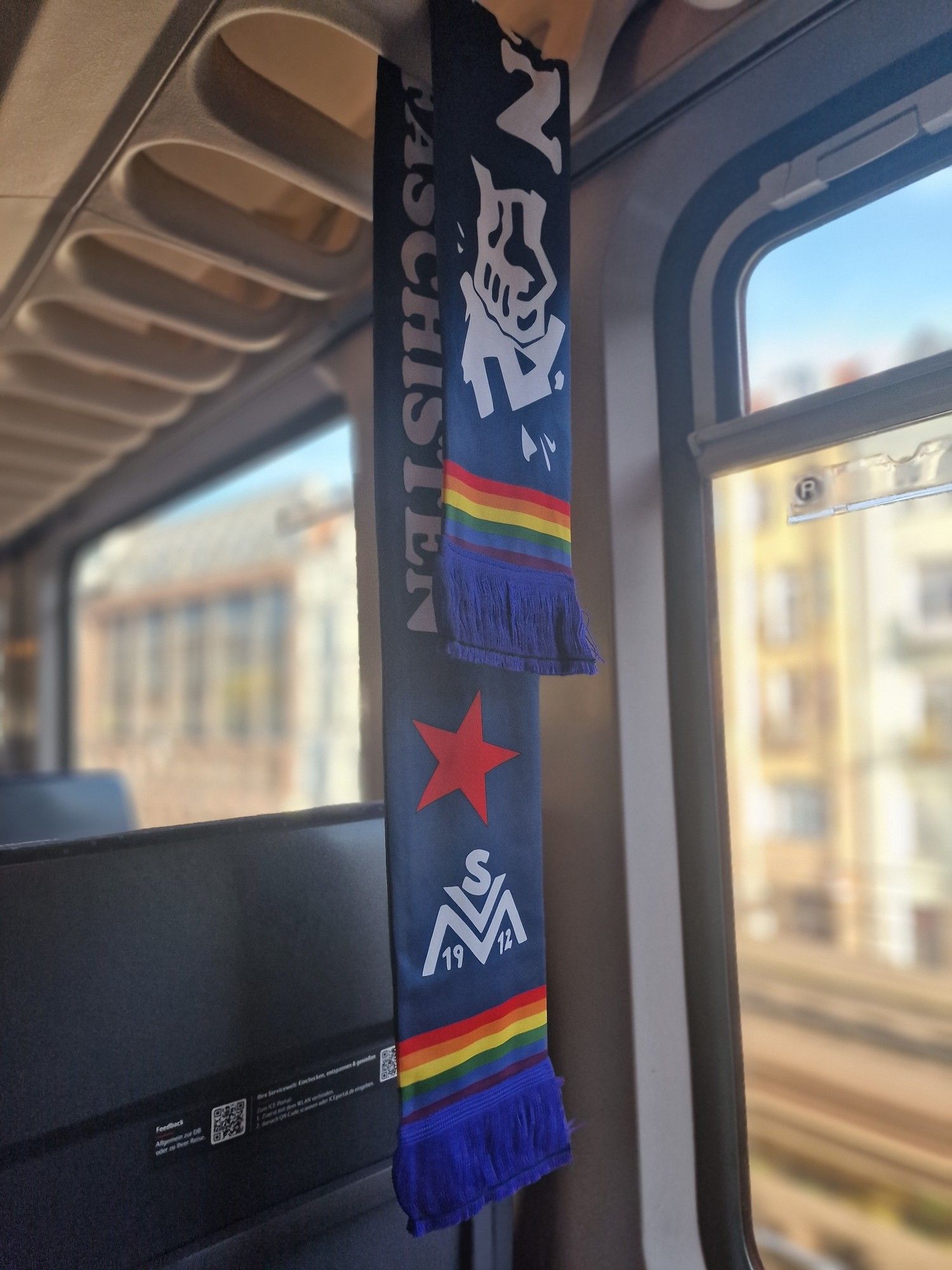 Foto eines SV Meppen Schal mit Regenbogenflagge, Roten Stern und einer Faust die ein Hackenkreuz zerstört.