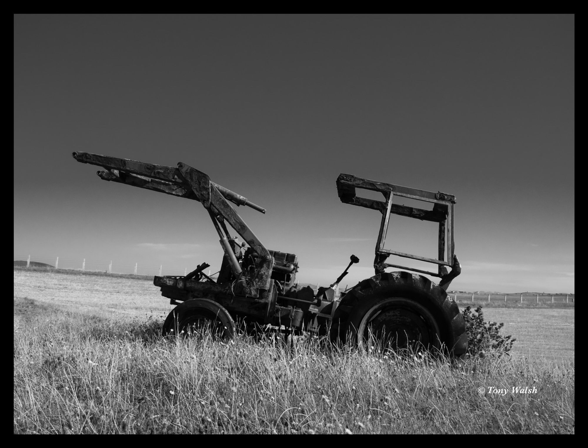 Monochrome image of a rusted remains of a tractor in a field on North Uist on a bright sunny day