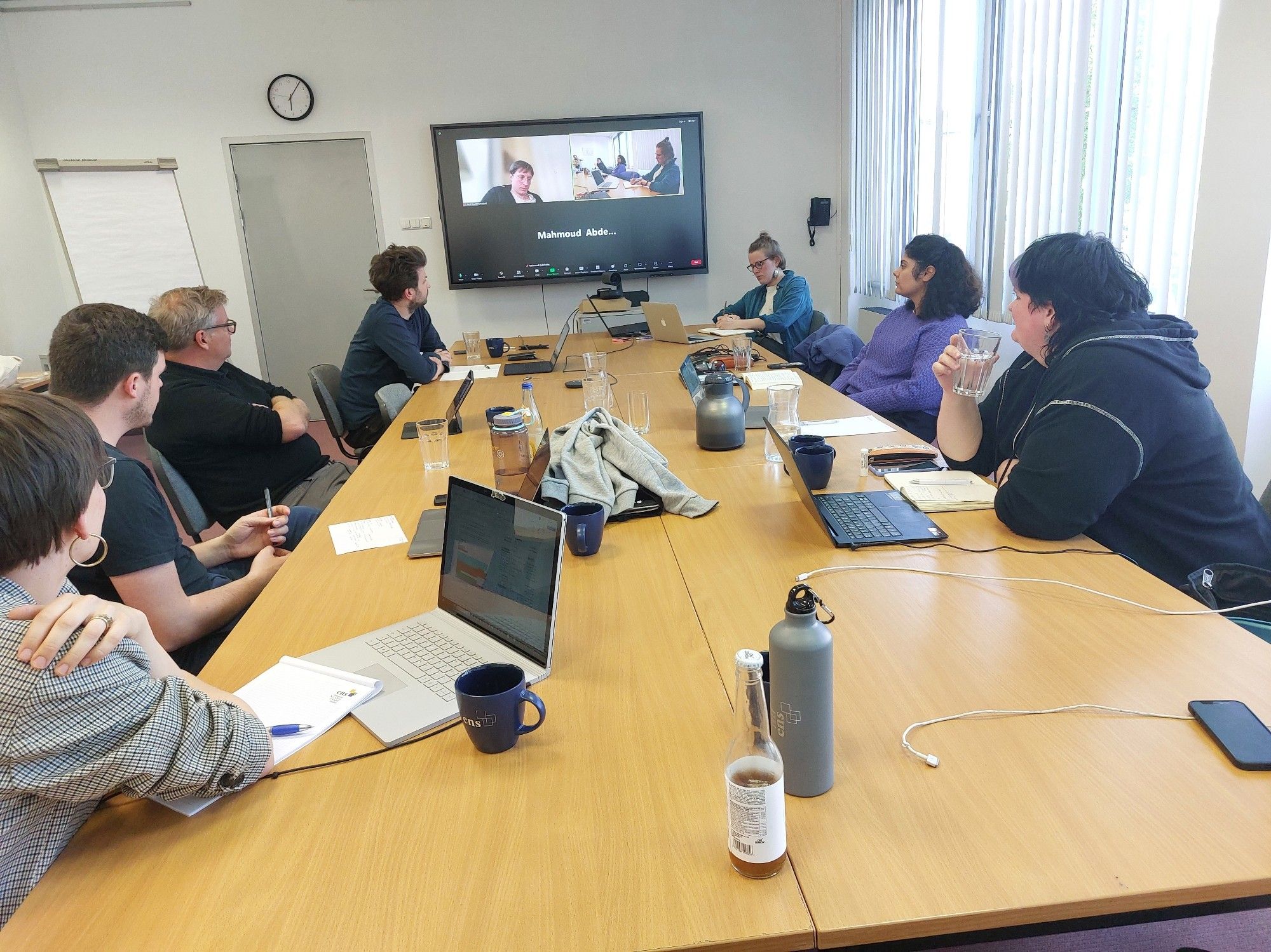 Our grouped sitting at a roundtable staring on a hybrid meeting devicr, listening closely to a presentation.