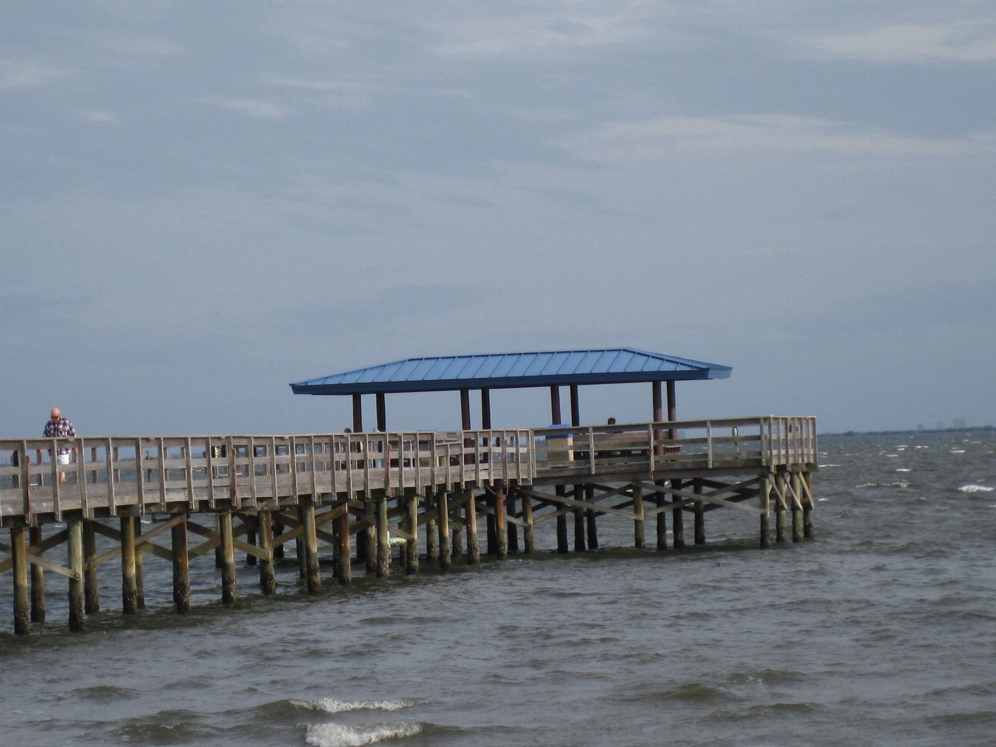 Pier with covered shelter at the end, overlooking a bay, home to fish, dolphins, manatees, and small craft boats, fishermen, and bay watchers