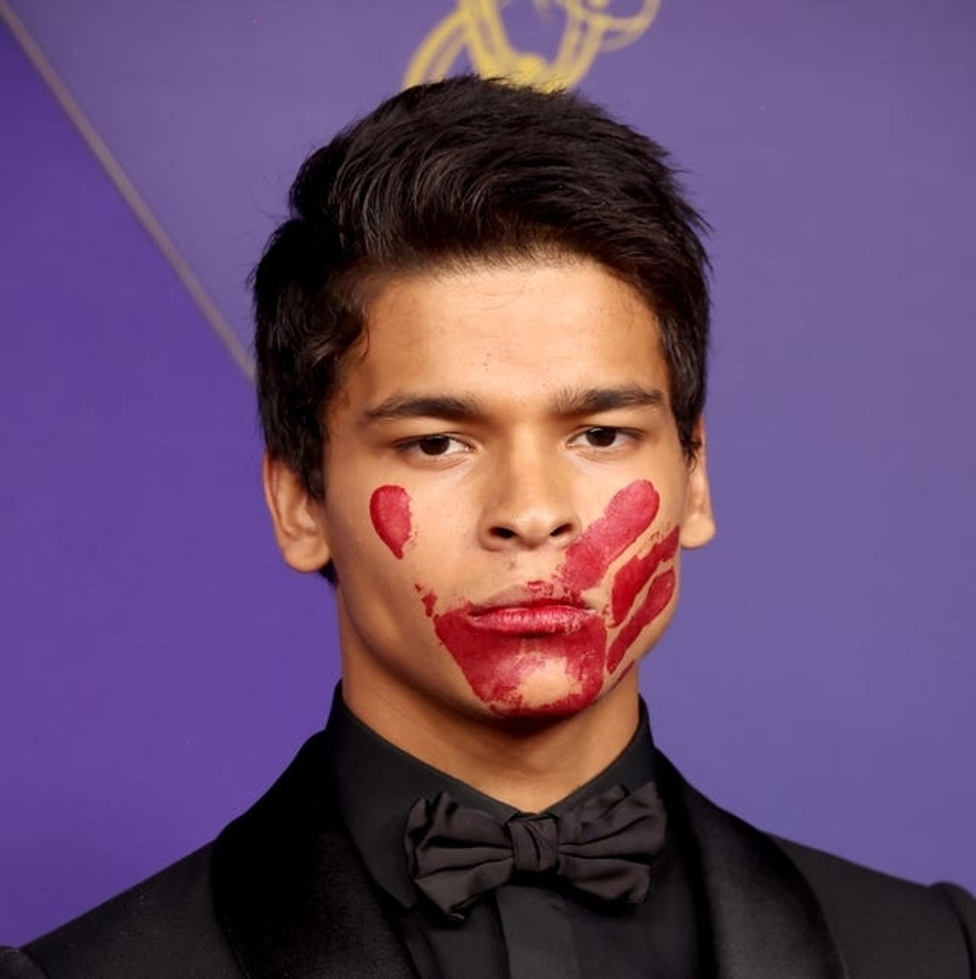 Actor D'Pharaoh Woon-a-Tai in an all black suit and bowtie, with a red handprint over his mouth symbolizing missing and murdered Indigenous women and girls