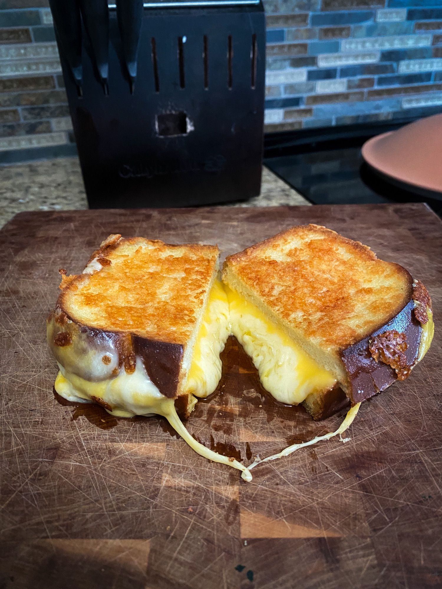 a perfectly toasted grilled cheese cut in half on a cutting board. two strands of melted cheese make the sandwich appear to be holding hands