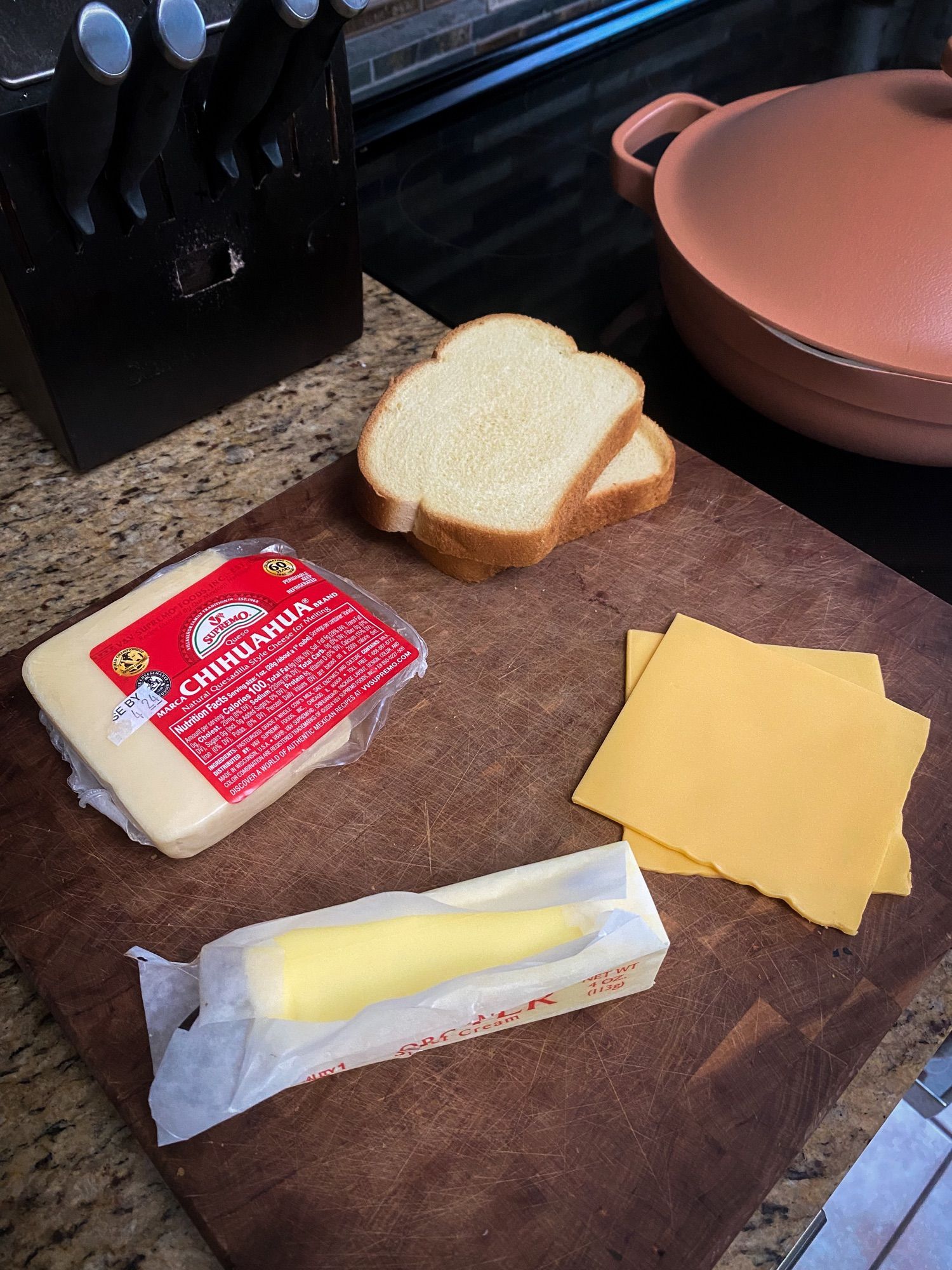 the ingredients for a grilled cheese on a cutting board; american & chihuahua cheese, butter & bread