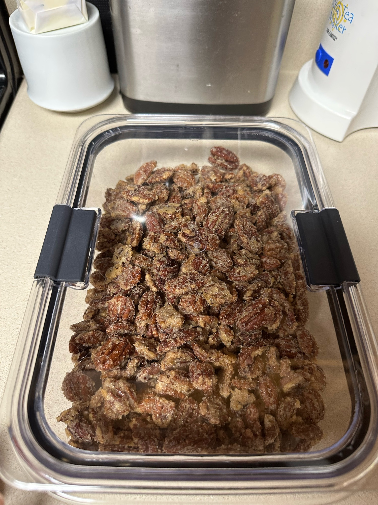 A clear kitchen storage container full of about a pound of candied pecans. 