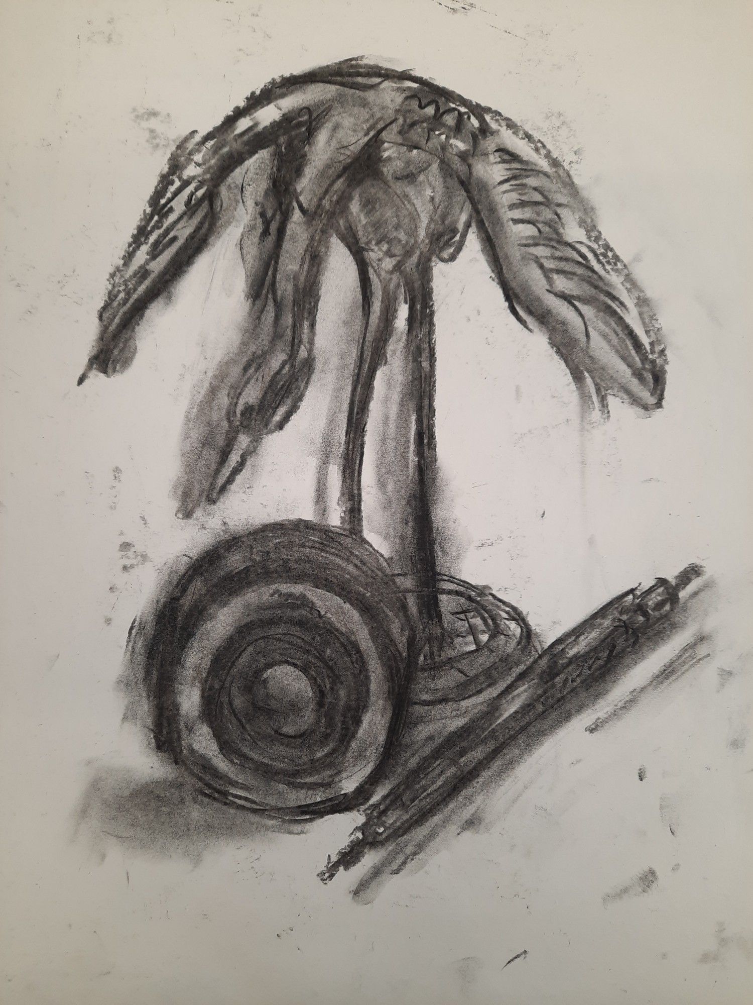 a charcoal sketch of a crane figurine with its wings outstretched and its neck pointing downwards. it has really long and straight legs. to the right of it is a rotring 600 and in front is a camera lens but it doesn't really look like a camera lens.