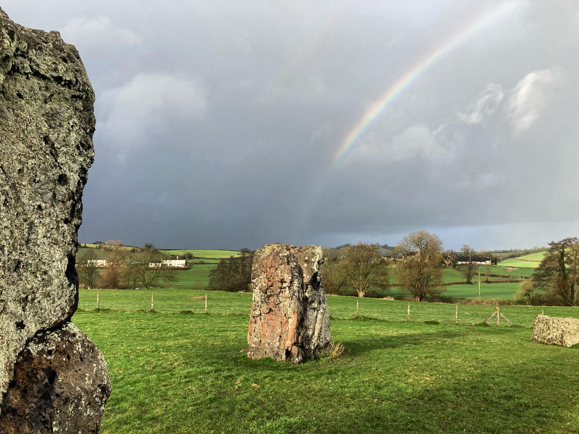 Rainbow over Stanton Drew stone circle against a a dark stormy sky