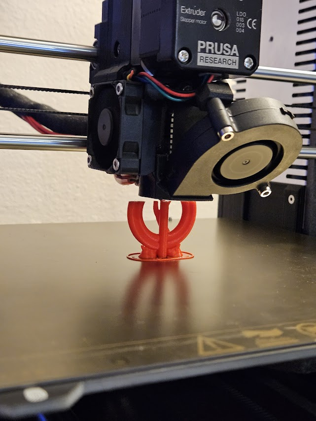 A 3D printer spitting out a Nier cosplay button in orange filament