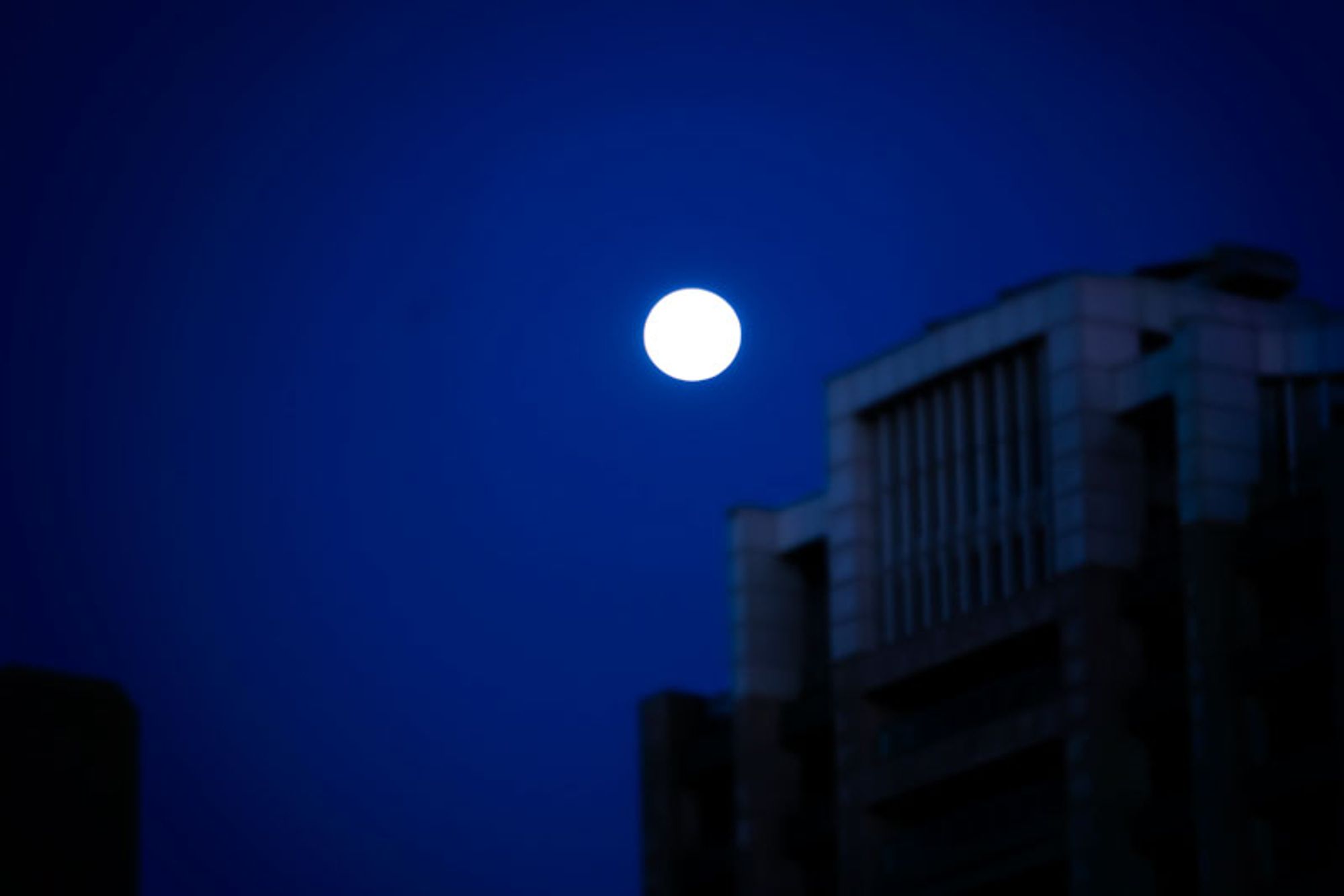 A full moon at night above some urban buildings