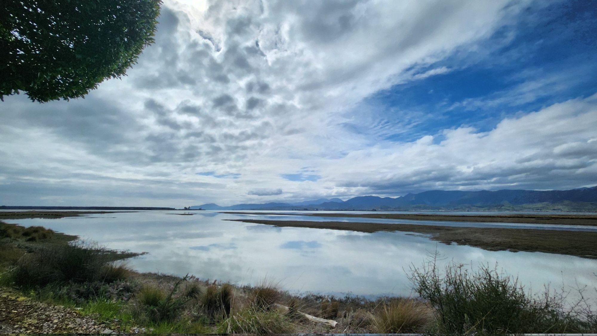 View across Waimea Inlet in Nelson with streaks of cloud and deep blue sky reflected in still waters