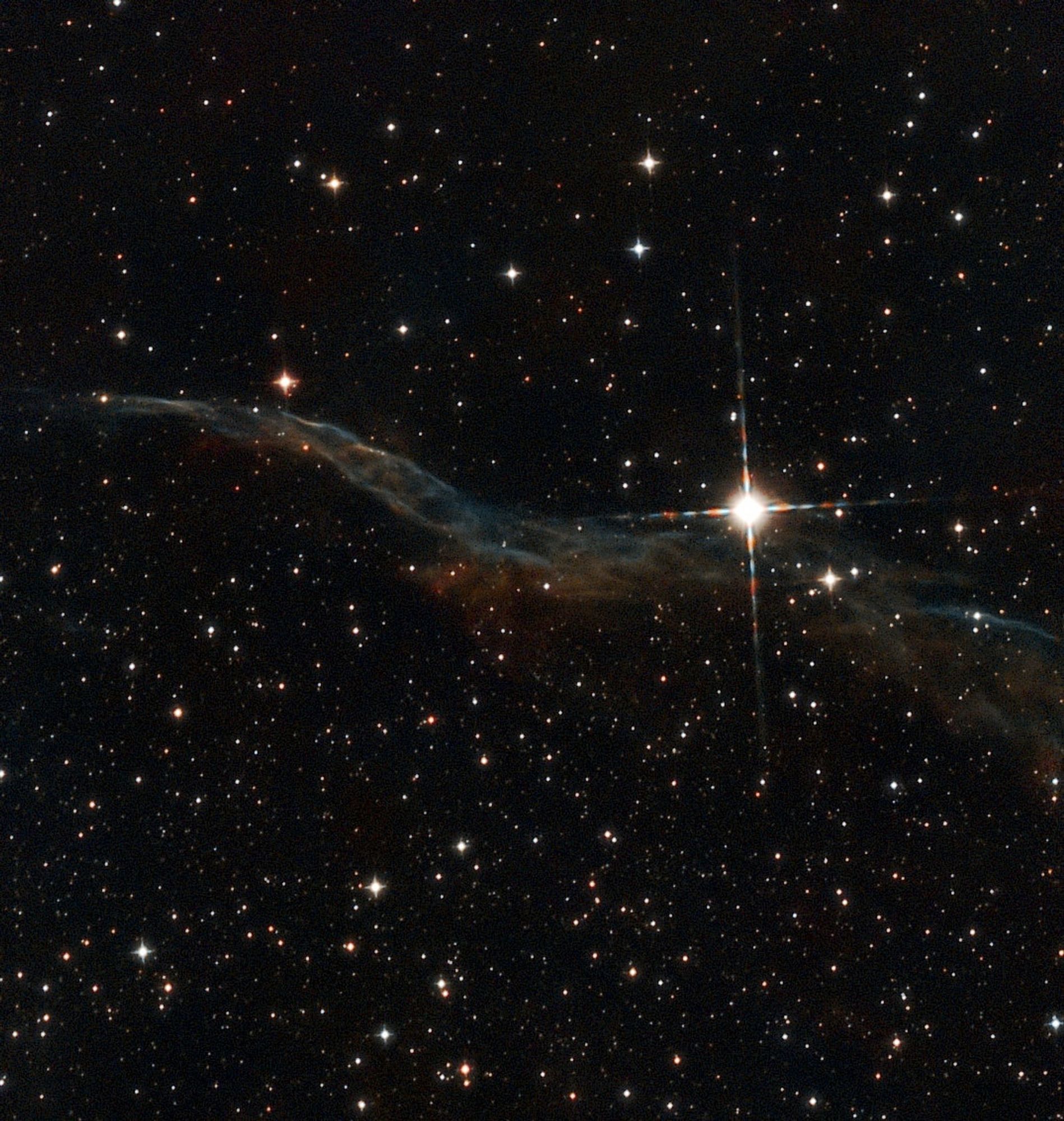 The Veil nebula, a thin blue and orange wisp across the image with a bright spiky star in front