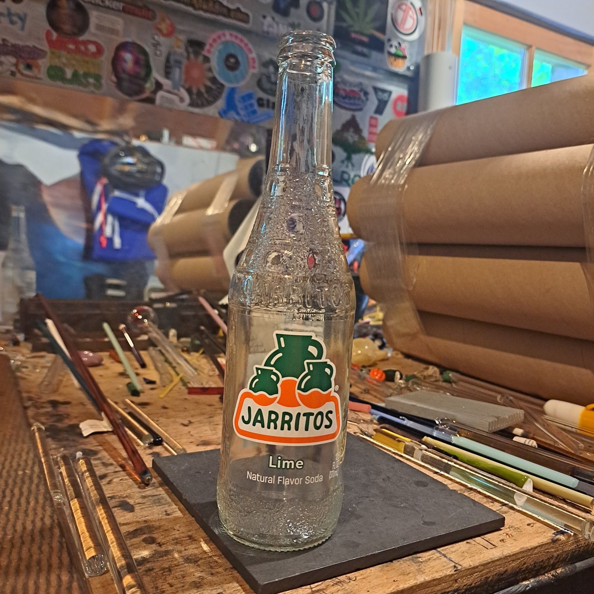 An empty glass Jarritos lime soda bottle stands on a lampworking bench.