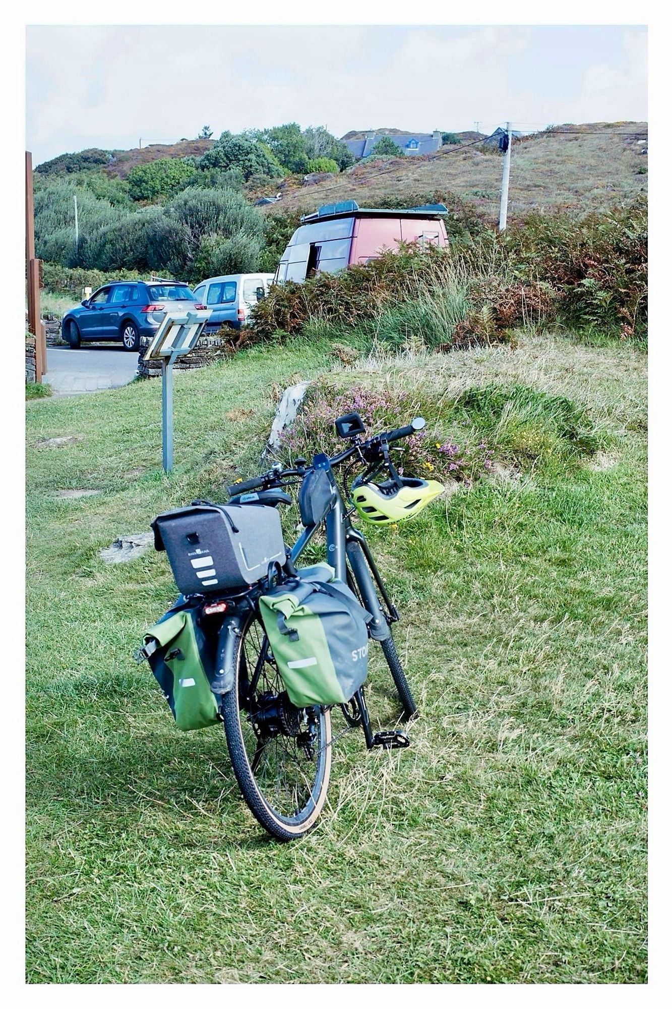 My bike with panniers parked on the grass in the foreground, with a couple of cars and a red camper van in the carpark at the Altar Wedge Tomb.

I stopped here mainly for a little break from the headwind. That didn’t work. Those south westerlies were insistent.