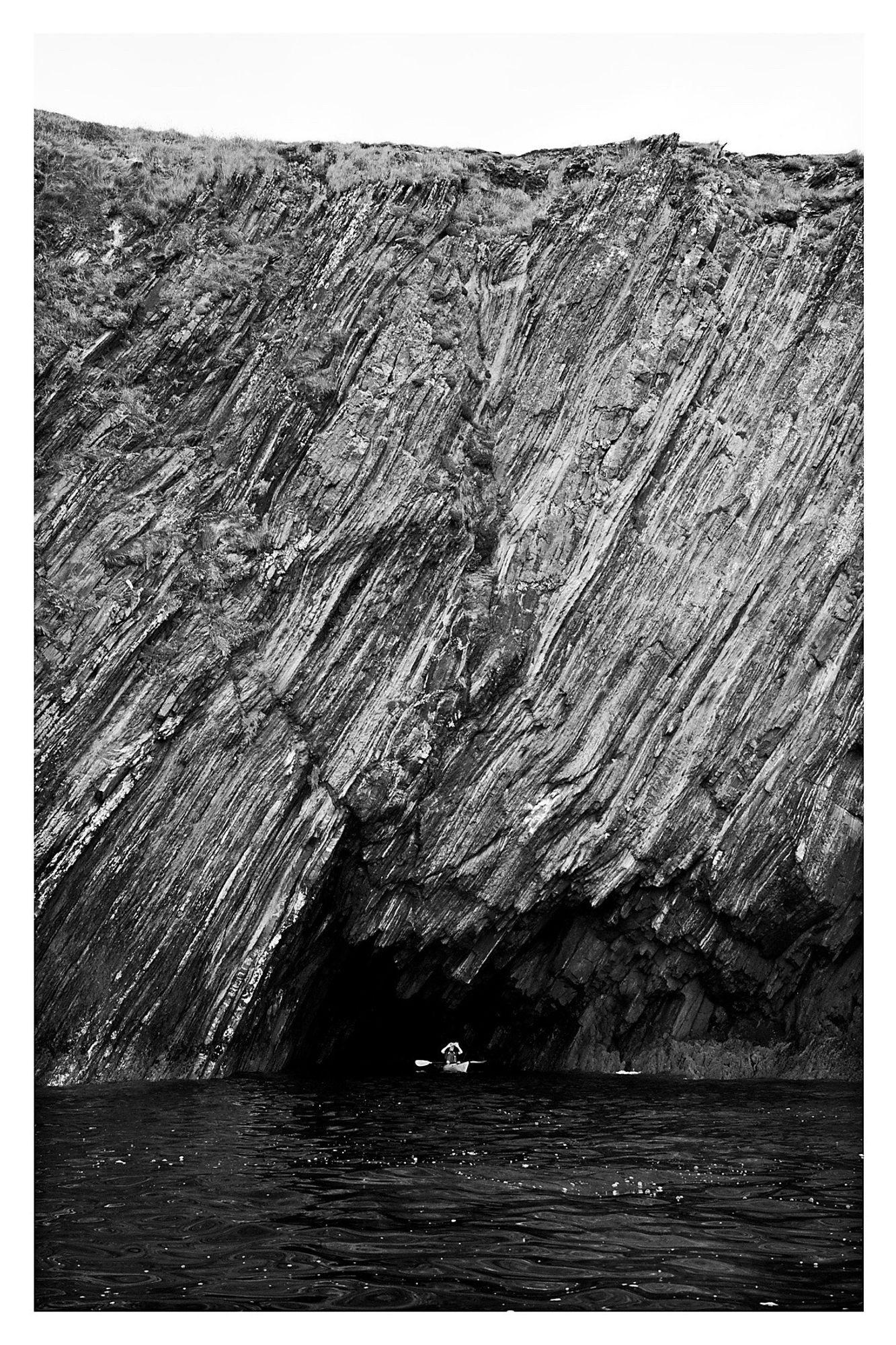 In the previous photo there’s a plateau on the profile of the island. Just visible from that distance are some caves. This is one of those caves below the plateau with a kayaker at the entrance for scale.

The rock strata has formed in near vertical sweeping lines, almost at ‘1 o’clock to 7 o’clock.’ If you like.