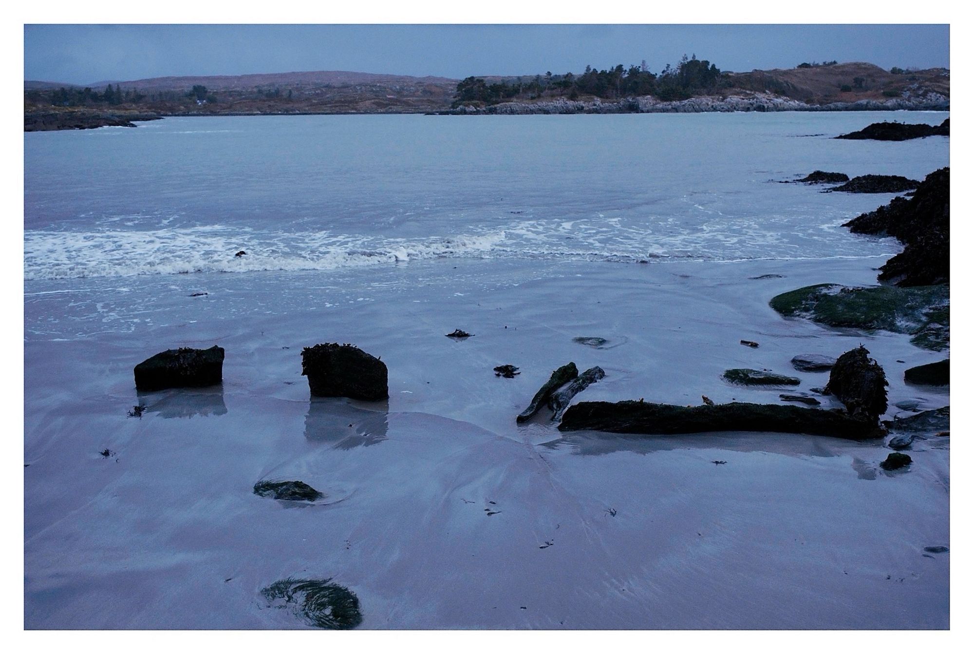 Description: On mid-foreshore at low water on S side of Ballyrisode
beach/strand (inner beach) to immediate SE of carpark; site would cover at mid to high water. Eroded and well buried, so difficult to assess nature and extent. 2 upright slabs at slight angles to each other facing seaward and may have been a third stone but is now collapsed; 1m to south 3 long slabs enclosing a rectangular box-like stone setting; enclosed on 3 sides and open on side facing seaward. May be an earlier site reused for later burials. Potential fulacht fiadh stone trough or a cist burial.