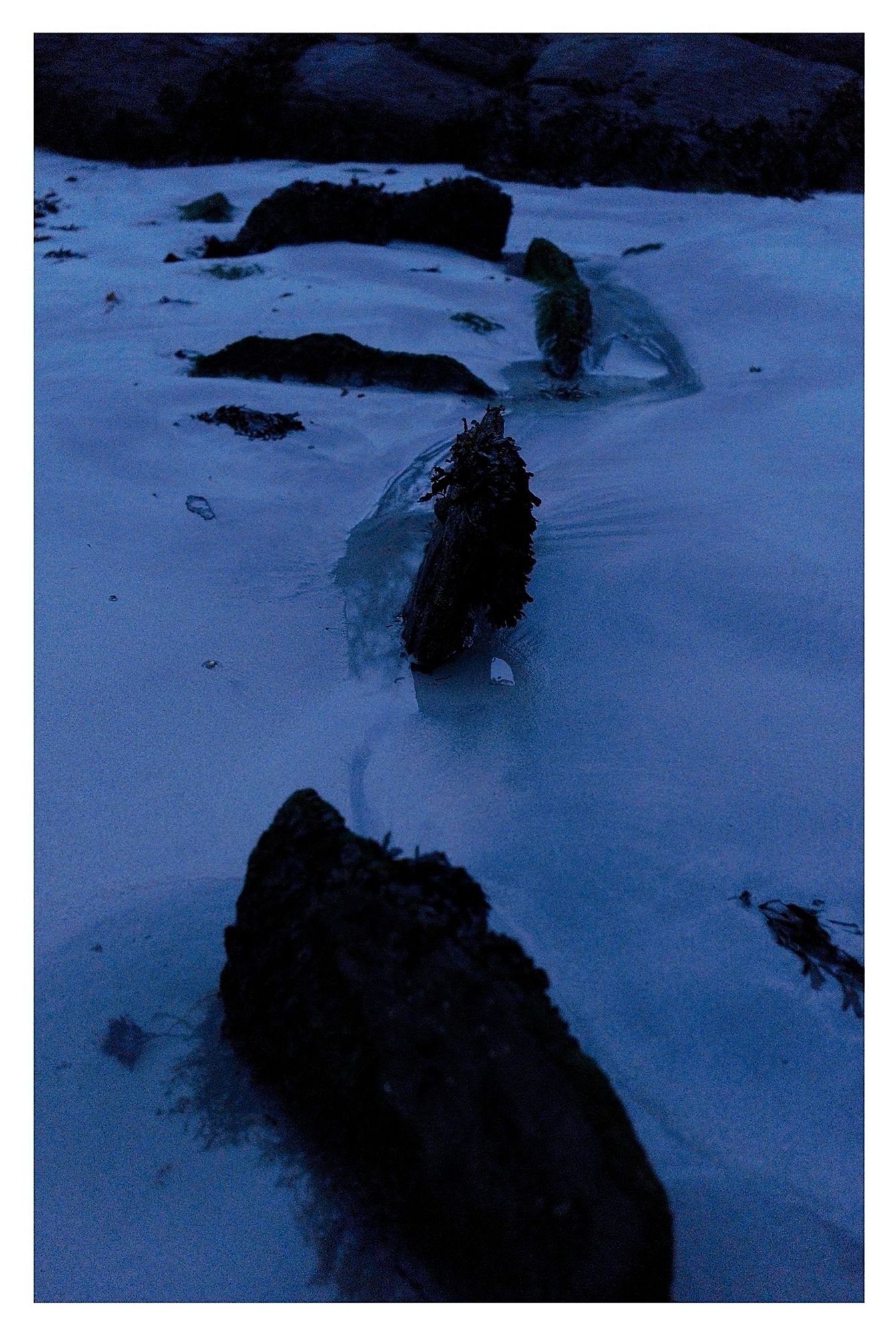 Description: On mid-foreshore at low water on S side of Ballyrisode
beach/strand (inner beach) to immediate
SE of carpark; site would cover at mid to high water. Eroded and well buried, so difficult to assess nature and extent. 2 upright slabs at slight angles to each other facing seaward and may have been a third stone but is now collapsed; 1m to south 3 long slabs enclosing a rectangular box-like stone setting; enclosed on 3 sides and open on side facing seaward. May be an earlier site reused for later burials. Potential fulacht fiadh stone trough or a cist burial.