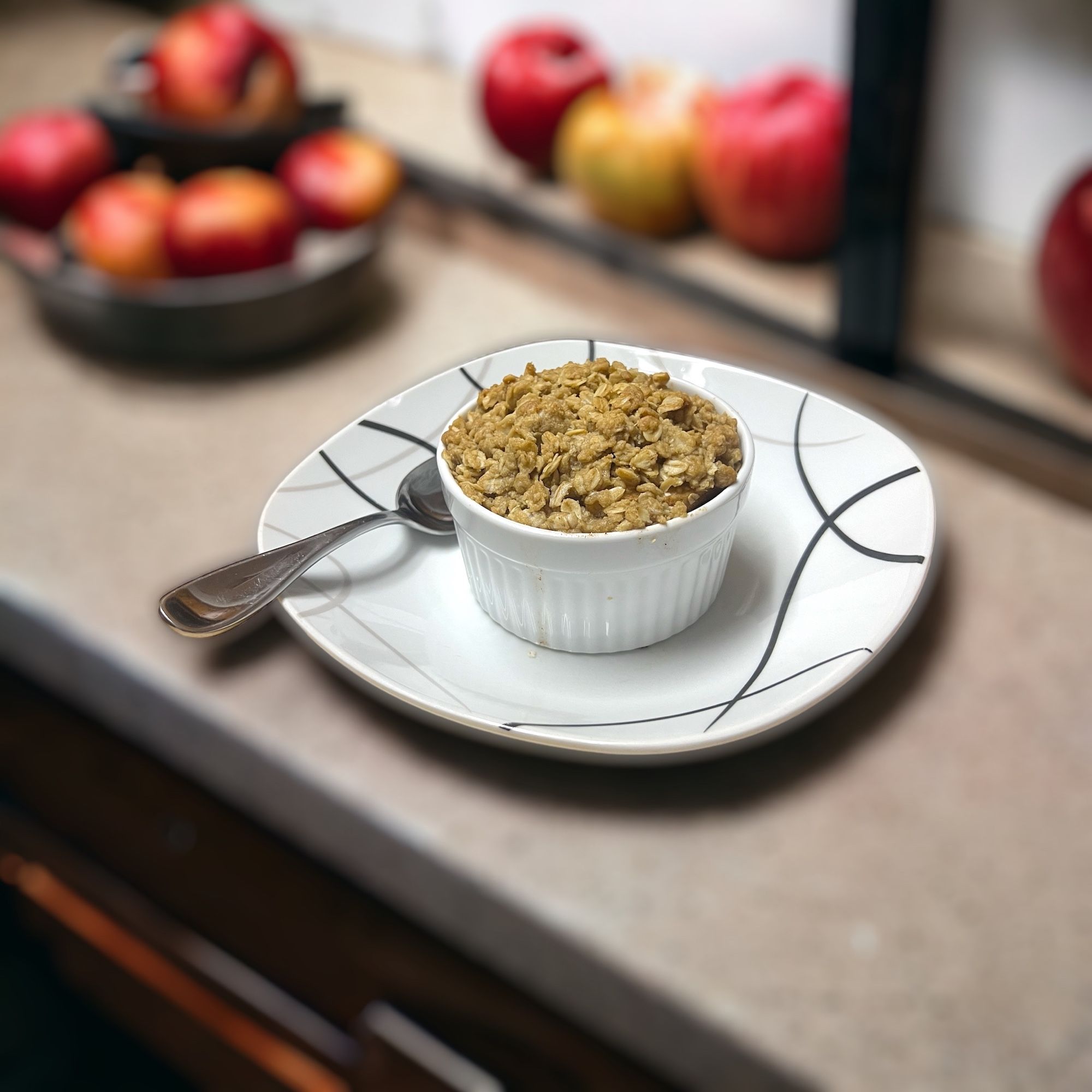 Apple crisp in a white ramekin on a plate with a spoon