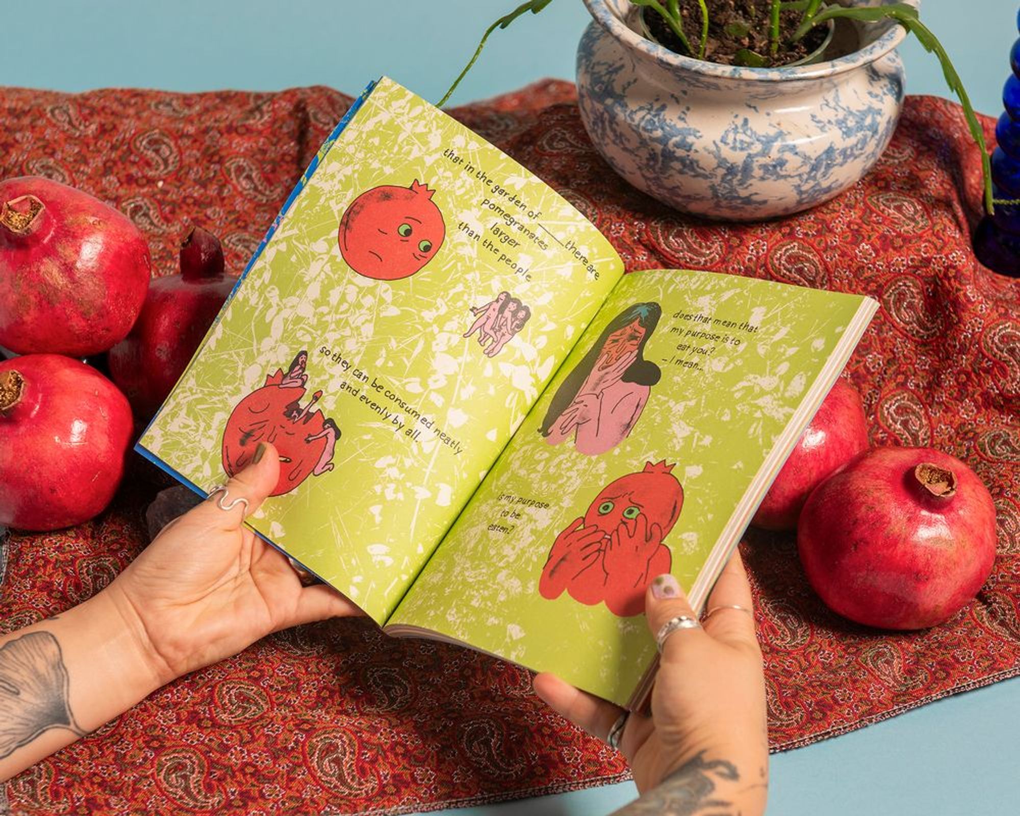 turning the pages of WHEN TO PICK A POMEGRANATE by Yasmeen Abedifard. Text reads: That in the garden of ____there are pomegranates larger than the people. So they can be consumed neatly and evenly by all. -Does that mean that my purpose is to eat you?- Is my purpose to be eaten?