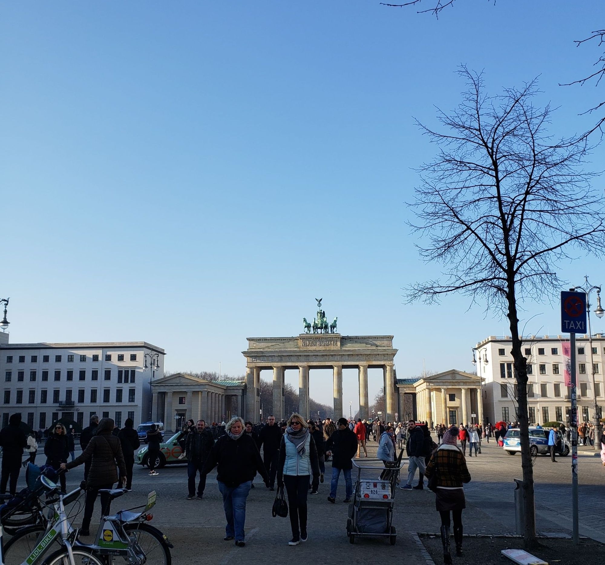 The Brandenburg Gate on a clear winter day. There are lots of pedestrians walking through the plaza.