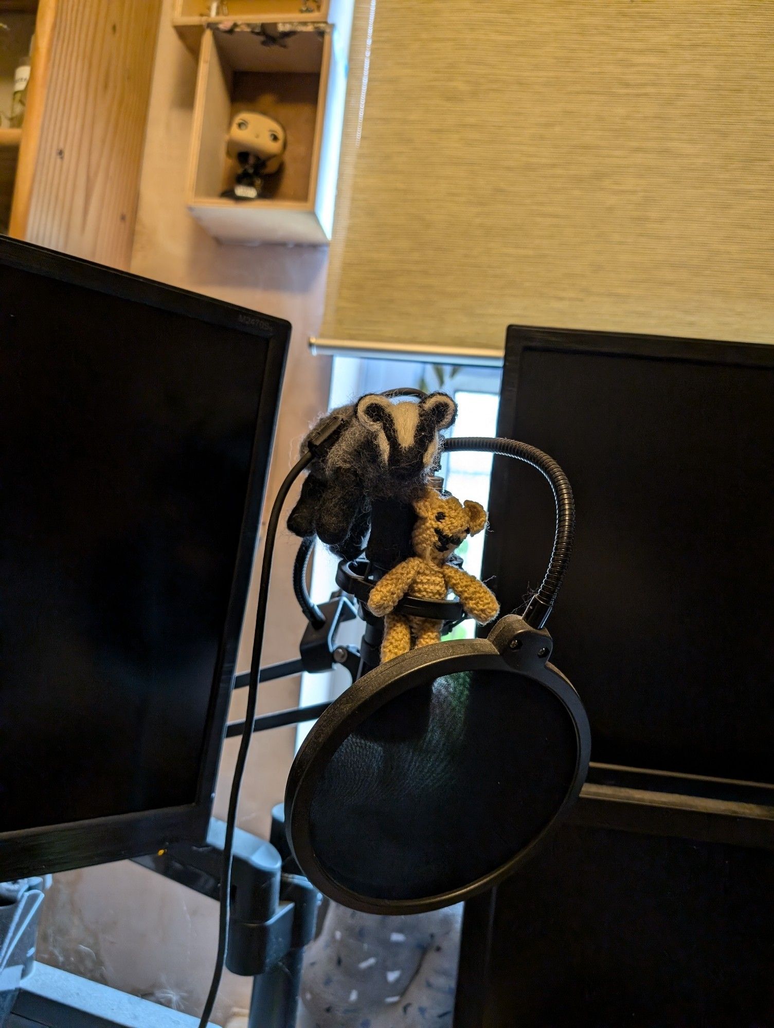 A condenser microphone, with pop filter, bracketed by screens. A little crochet bear and felted badger are in attendance.