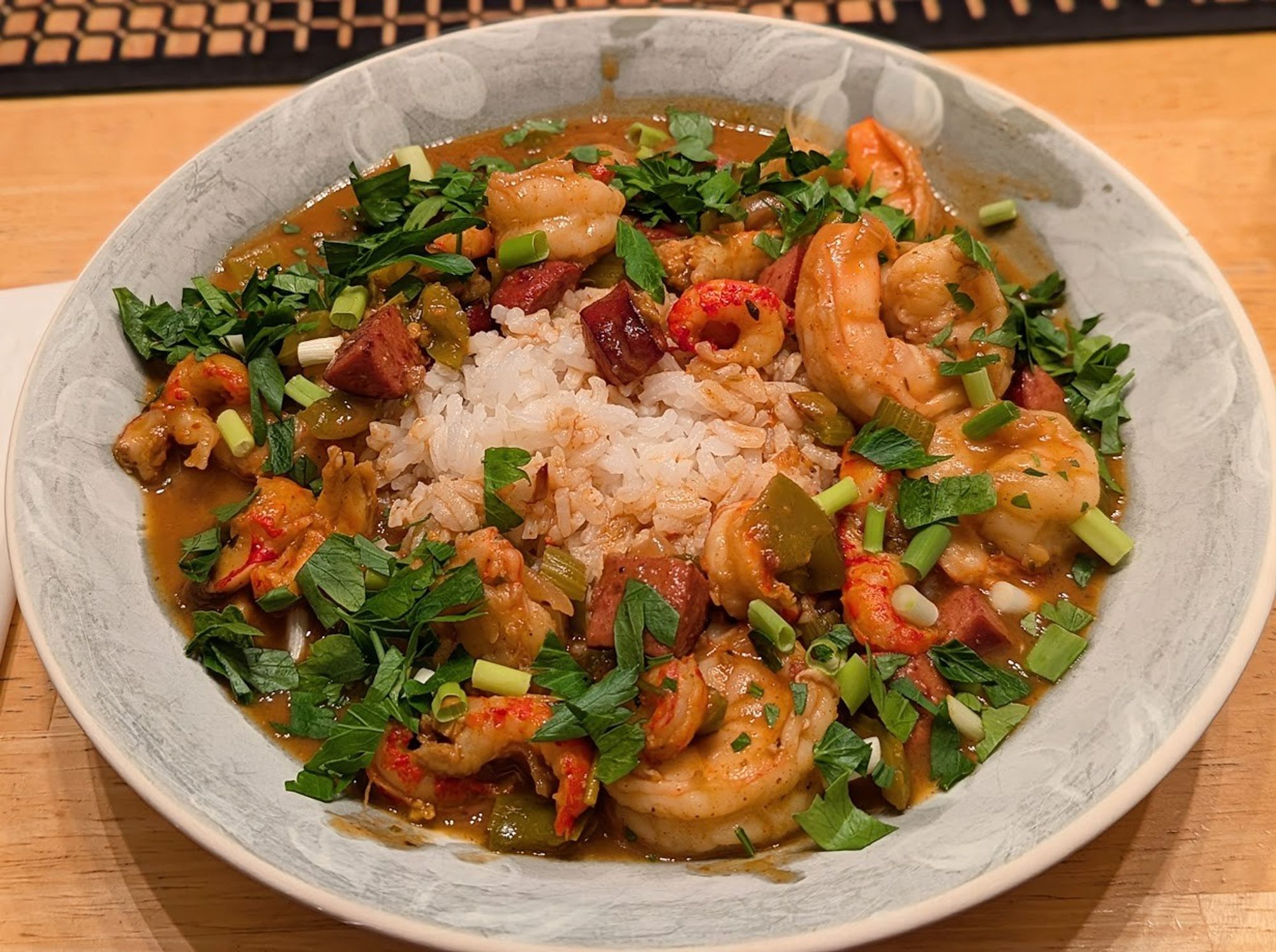 A green bowl.  There is a mound of white rice in the middle.  It is surrounded by a brown sauce full of shrimp, sausage, and crawfish.  It is garnished with scallions and parsley.