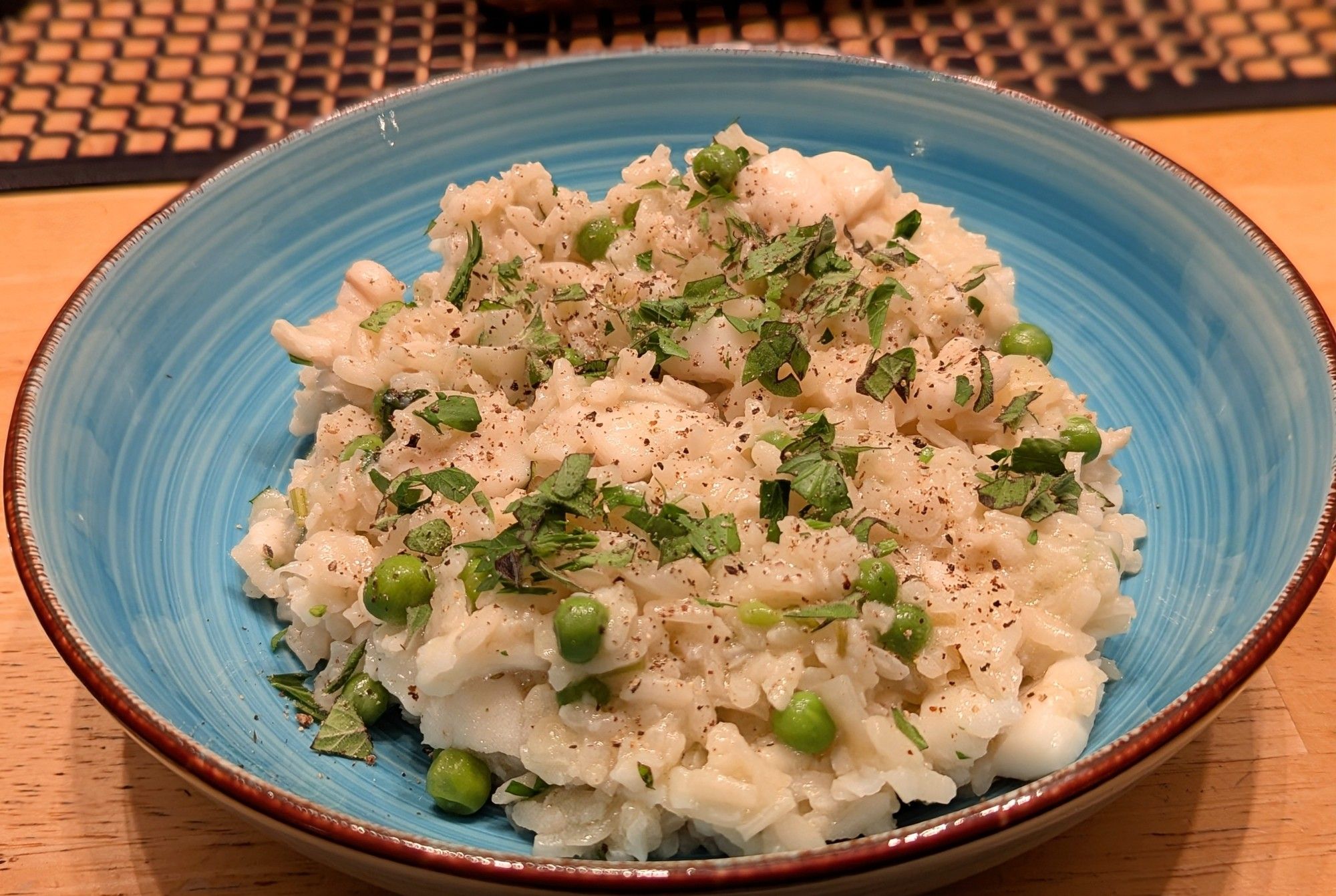 A light blue bowl with risotto of fish and peas, sprinkled with green herbs and black pepper.