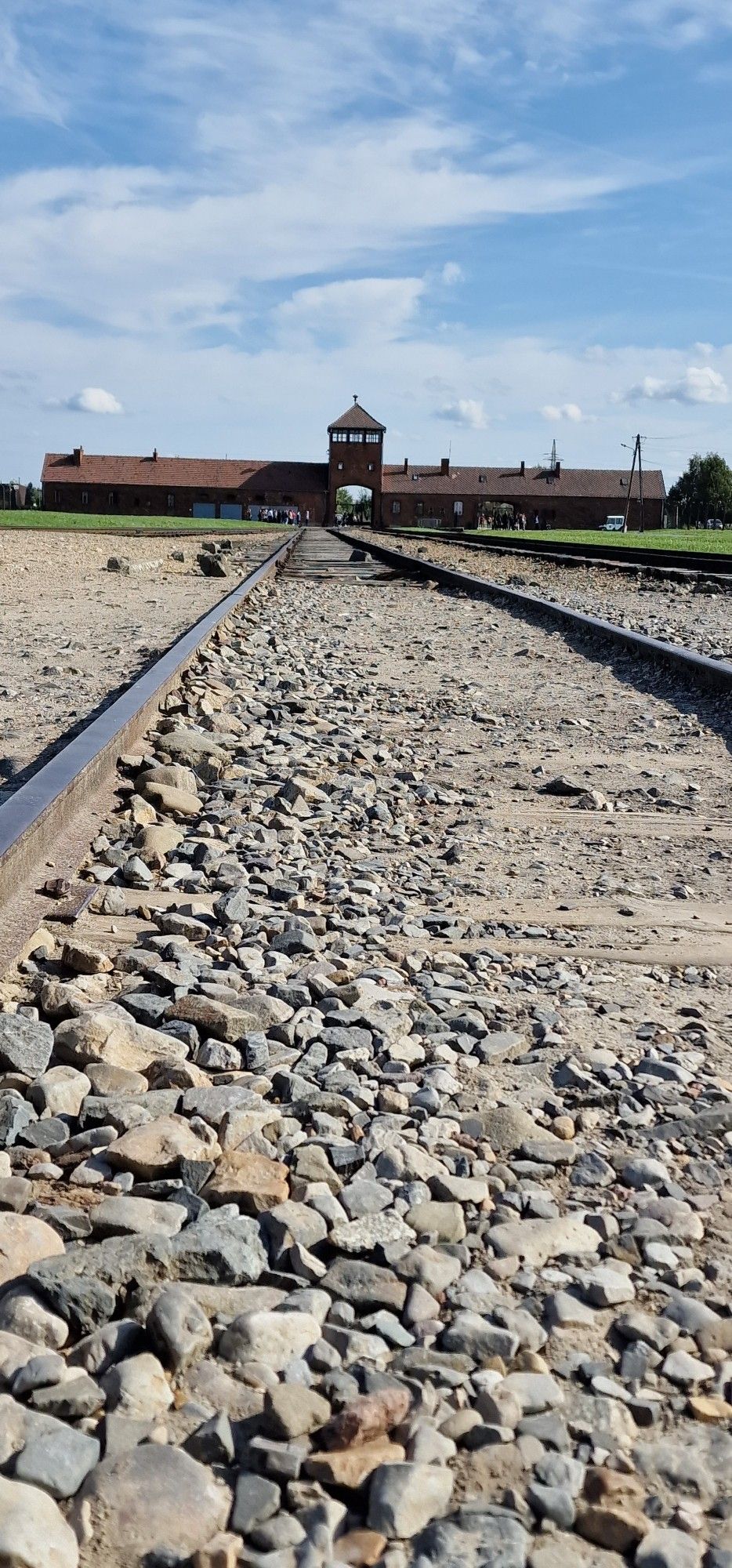 Bahnreise in der Mitte mit Schotter, am Ende der Gleise ist das Eingangsportal von Auschwitz Birkenau zu sehen