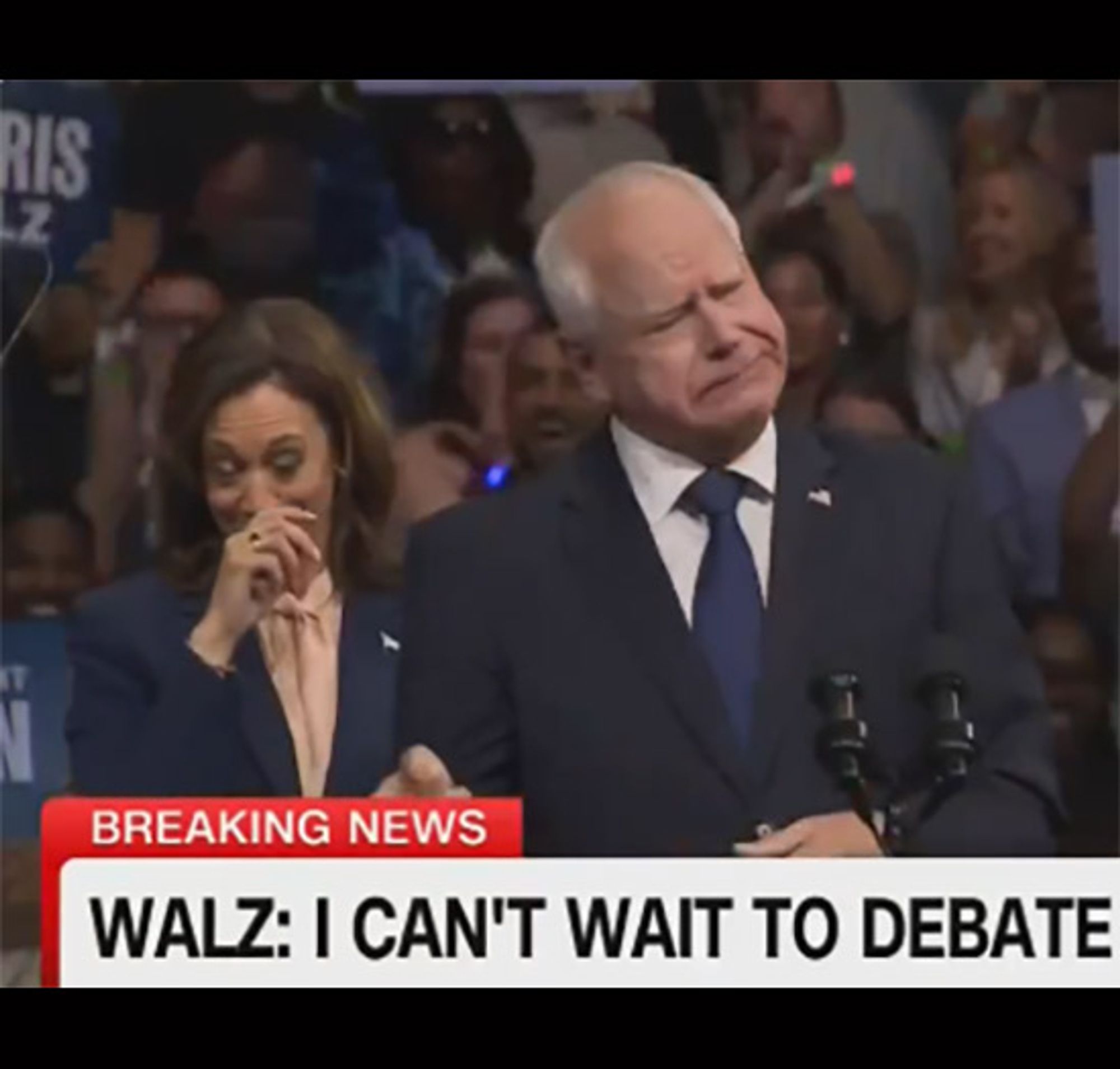 Harris and Walz on stage. Walz is doing Dad Joke Delivery face (rather like you've smelled a stinky fish) while Harris is slightly behind him, one hand pressed to her mouth as she tries not to laugh.