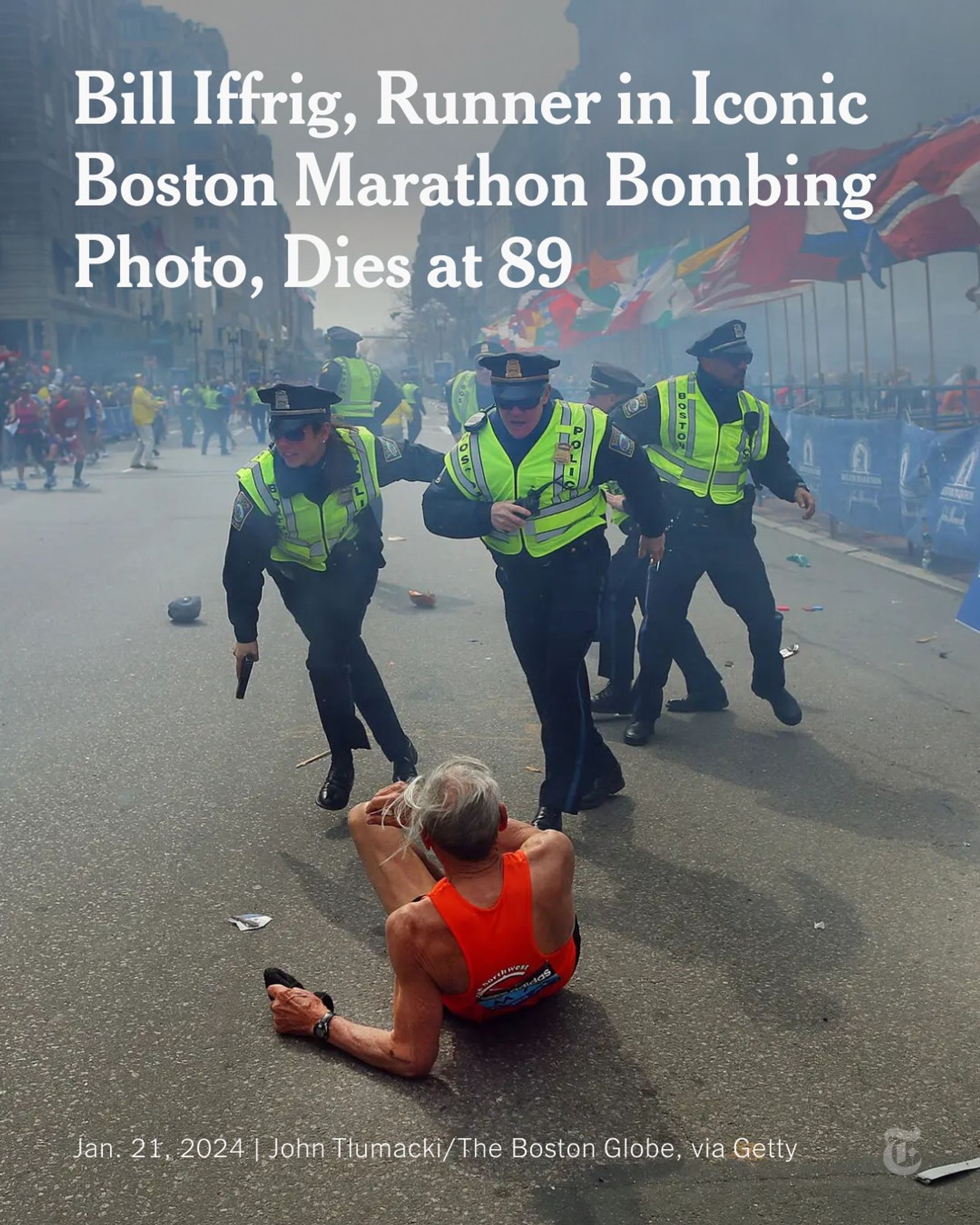 A person in an orange tank top on the street facing away as police officers in yellow vests run toward him. Flags and crowds of people line the street. A headline reads: "Bill Iffrig, Runner in Iconic Boston Marathon Bombing Photo, Dies at 89." Photo by John Tlumacki/The Boston Globe, via Getty Images.