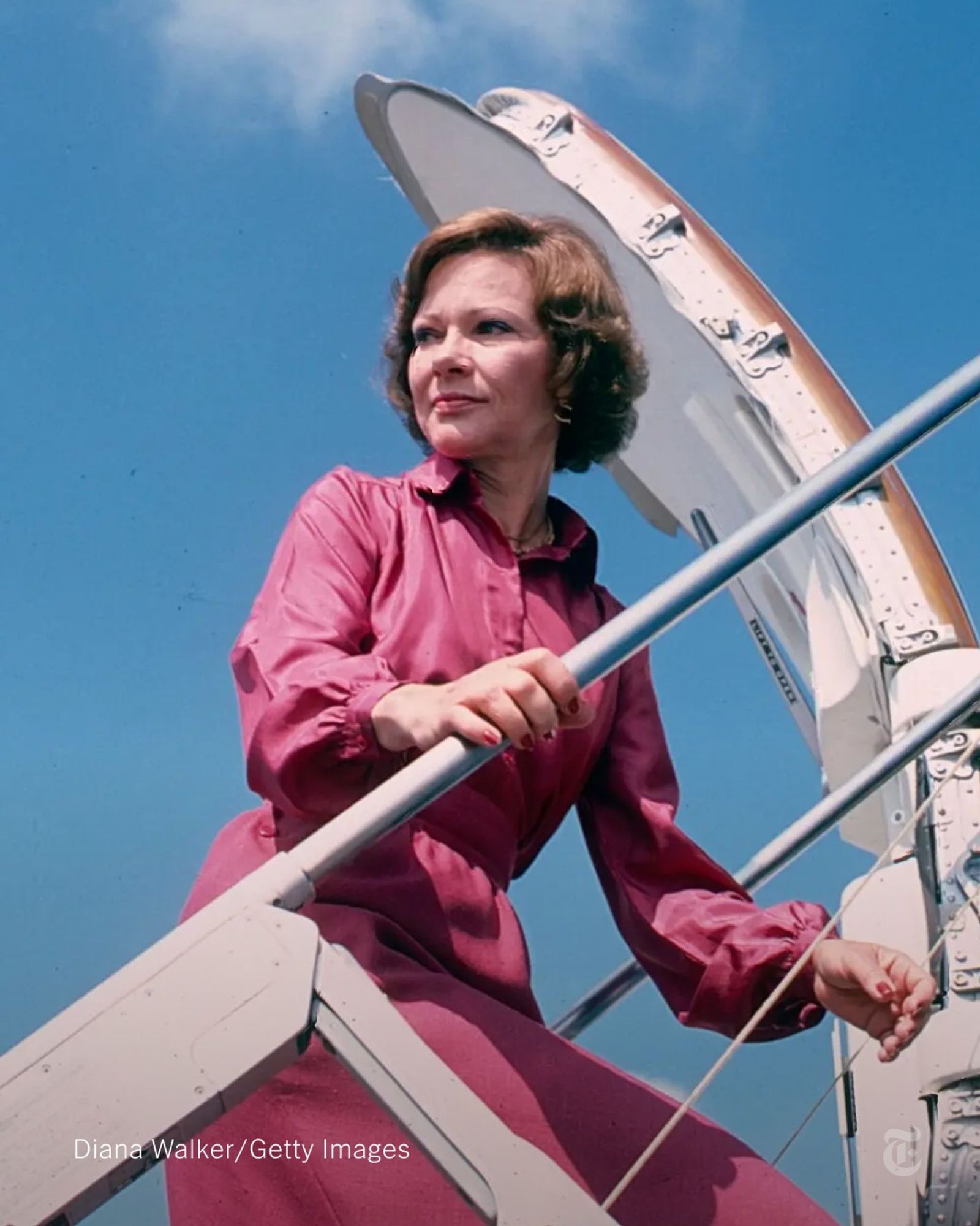 Rosalynn Carter, wearing a pink dress, climbs aboard a plane. Photo credit: Diana Walker/Getty Images.